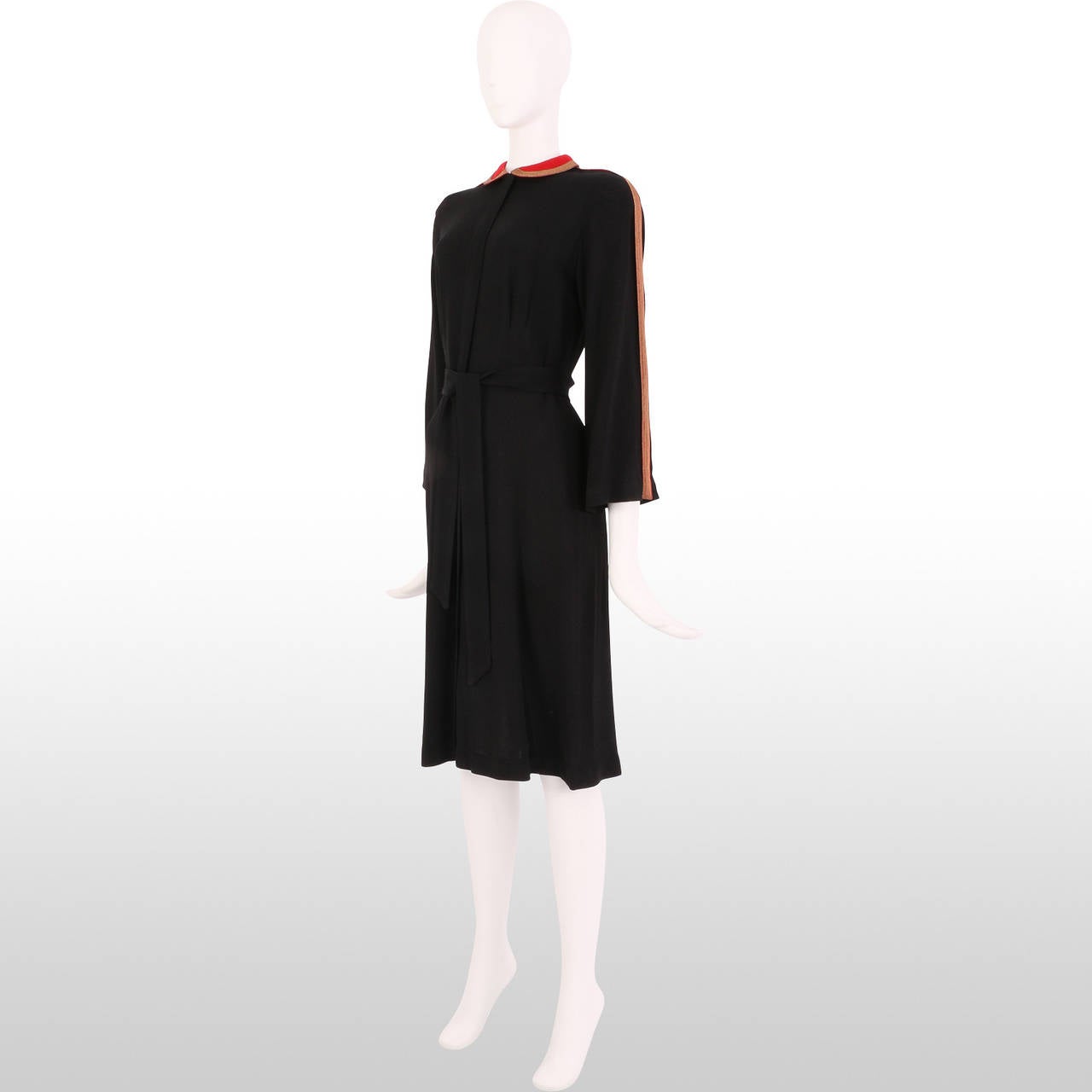 This gorgeous 1930's dress is a made from elegant black crepe fabric that drapes beautifully. This simple dress is given bold detail with the pillar box red peter pan collar and the gold and red metallic trim that lines collar and the sleeves. These