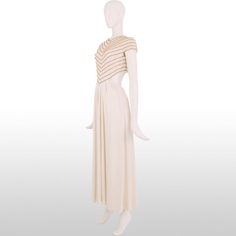This gorgeous gown is a 1970's piece by one of our favourite designers, Estévez . The bodice has elegant capped sleeves and is embellished with gold beading creating a chevron effect to the waist. The open back beings the real drama and the skirt