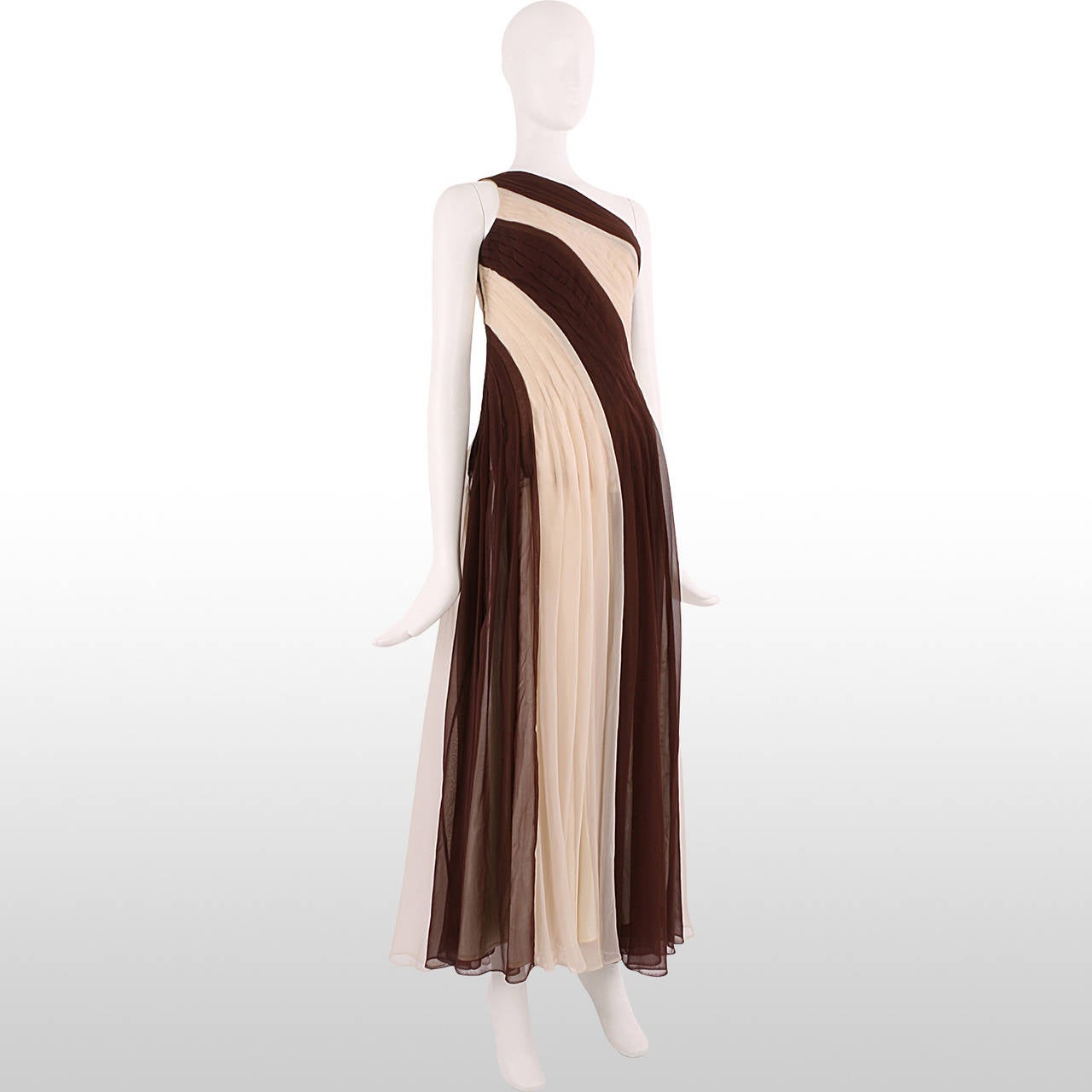 This fabulously elegant 1970's gown is made of alternating cocoa brown and ivory pleated chiffon that drapes from the asymmetric shoulder. The pleats form the structured bodice which then become loose at the waist to create a full flowing skirt. The
