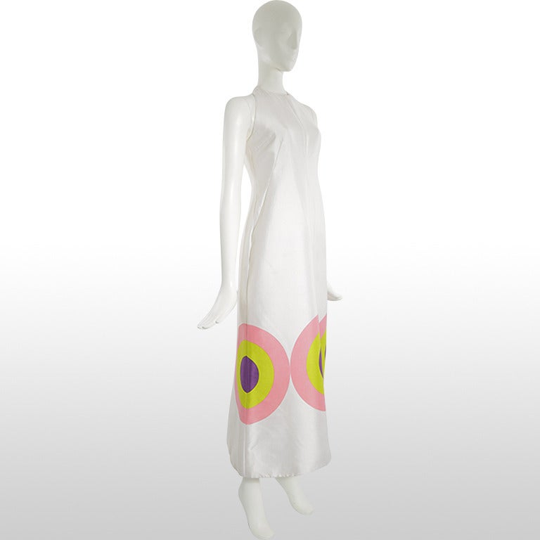 This 1960's gown incorporates classic vibrant design elements. The large bullseye motif circling the hem is what brings the real drama to the dress, drawing on the pop colours of pink, lime green and purple. The majority of the dress is a stark