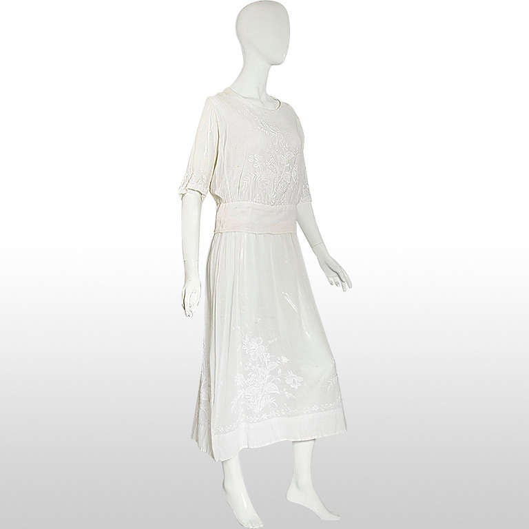 This classic 20's lawn dress comprises an underdress and a matching white blouse featuring floral embroidery cascading down the bottom of the dress. The blouse closes with snaps at the back. The underdress is loose fitting. We believe this dres