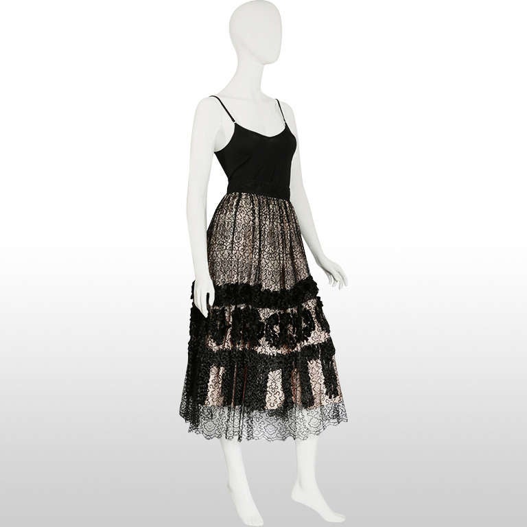We believe this skirt to have been made in the 50s. It is such a rare and special find. The underskirt is a pale blush pink sturdy satin. The black lace top skirt is unique in that the petite tassel detailing resemble tiny ponytails! The lace is