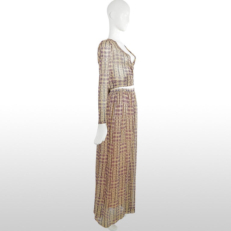 Sultry 1970's two-piece is made up of a cropped long sleeved wrap top and matching high waist maxi skirt.The piece features a metallic gold lurex fabric with a purple toned geometric print. The wrap top fastens with a tie at the back which creates a