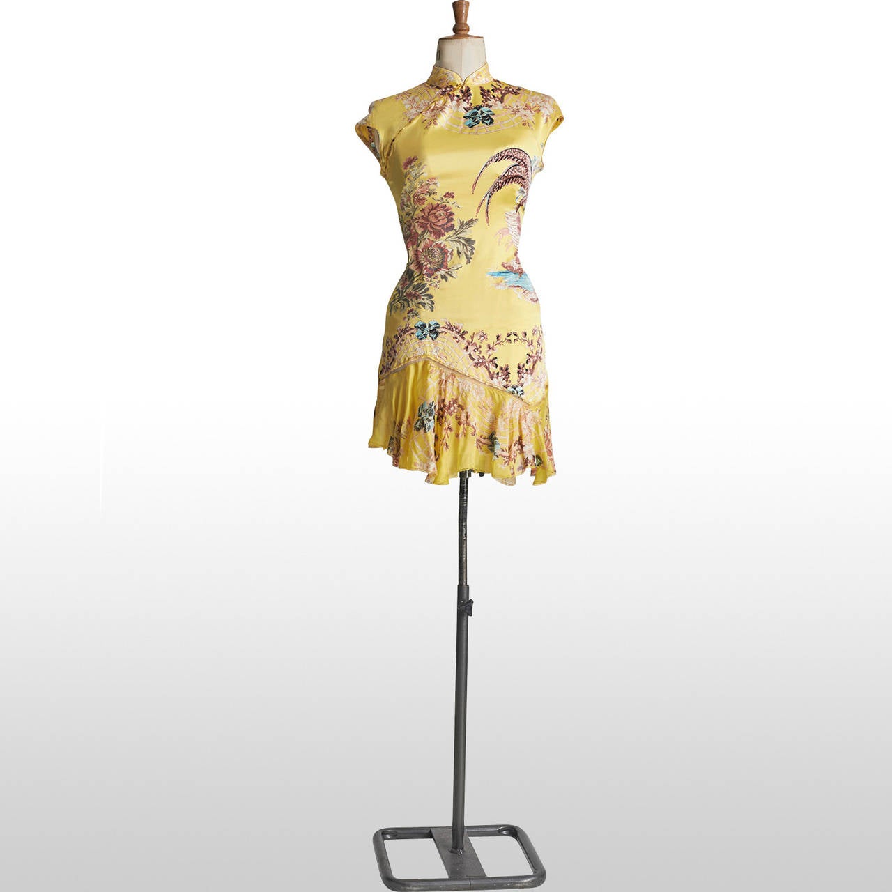 A Roberto Cavalli dress with Chinese flowers and  shimmering canaries encircling them is depicted against the yellow silk base of the fabric. The dress accentuates fine detailing as it features a built-in corset, gold hints of glitter on the flowers