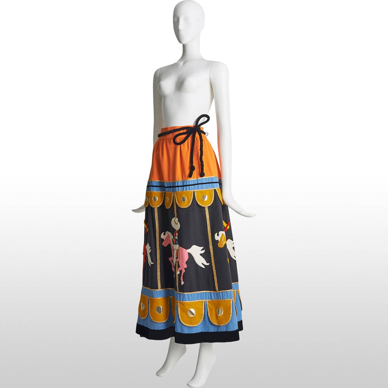 This is a very special piece from the 70s, exhibiting a carousel with people riding its horses, wearing traditional Mexican clothing. The skirt is made out of felt and cotton with metallic bradded trimming. The piece remains in excellent condition.