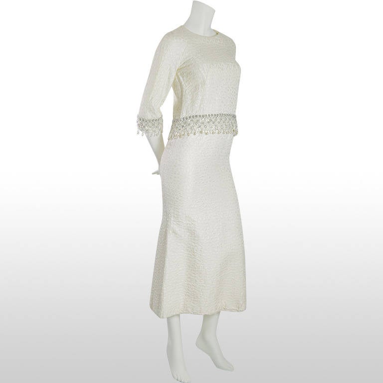 1960's ivory dress featuring a separate top that sits over the main dress, this is archetypal of this era. Beautiful ornate beading in silver and pearl line the hem and the cuffs of the jacket, which zips at the back. It is made from a gorgeous