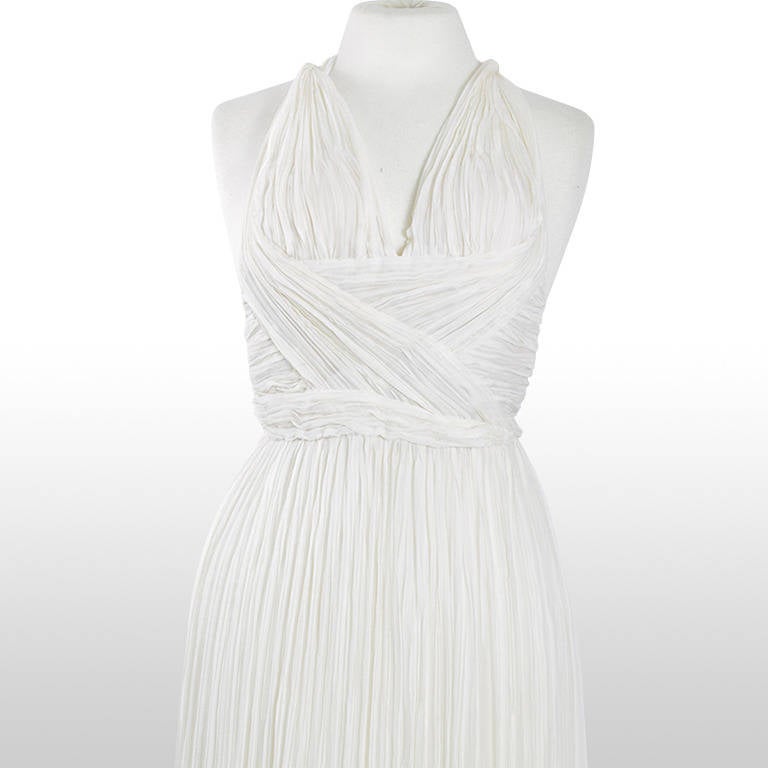 This gorgeous Ungaro gown is a couture piece made from pleated ivory silk chiffon. It has a Grecian influence with a feminine Marylin-esque floaty feel. It has a deep V neckline and sewn in bra cups to bring a fullness to its slim frame. It crosses