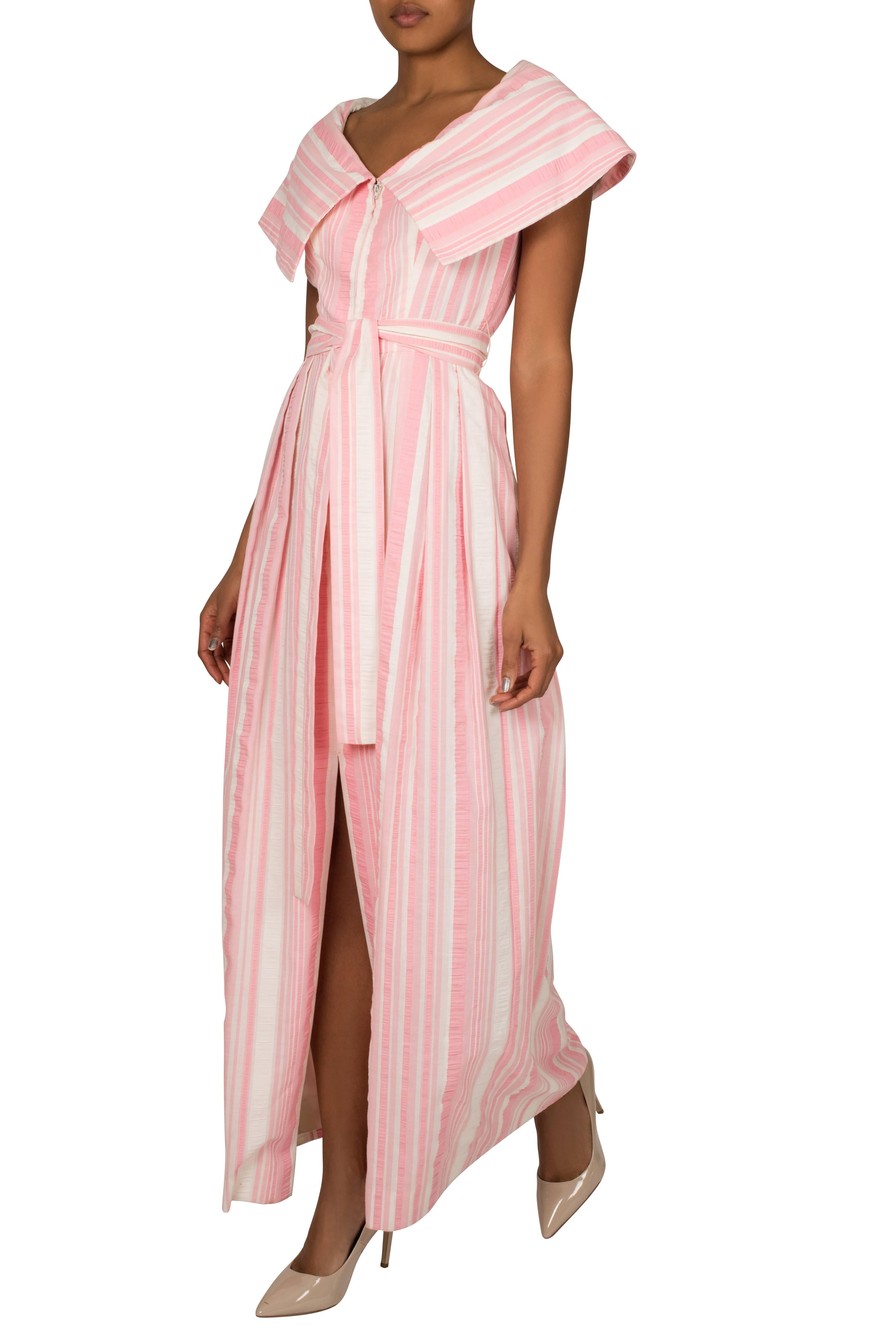 This cute 1970s Estevez V neck dress has a front zip opening with capelet style overlay around the shoulders. The fabric is a modern take on the classic pink seersucker stripe. The garment also features a matching tie waist belt, which accentuates