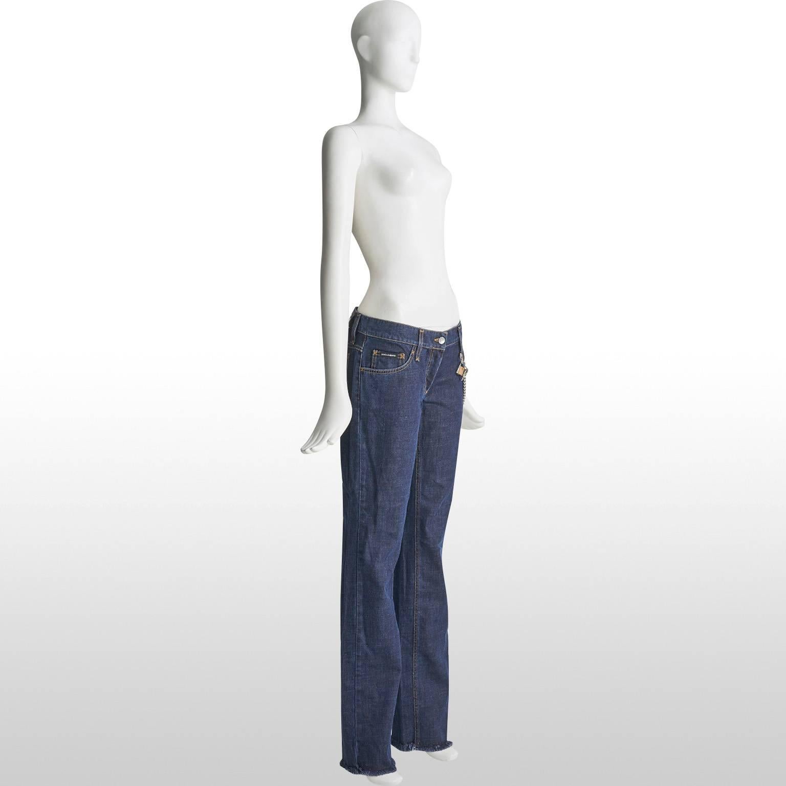 Brand new with tags, Dolce and Gabbana straight leg, mid blue denim jeans, frayed at the hem, with silver chain detail hanging around the hip and fastens with a padlock at the belt loop. The jeans sit comfortably on the hip and can also be worn with