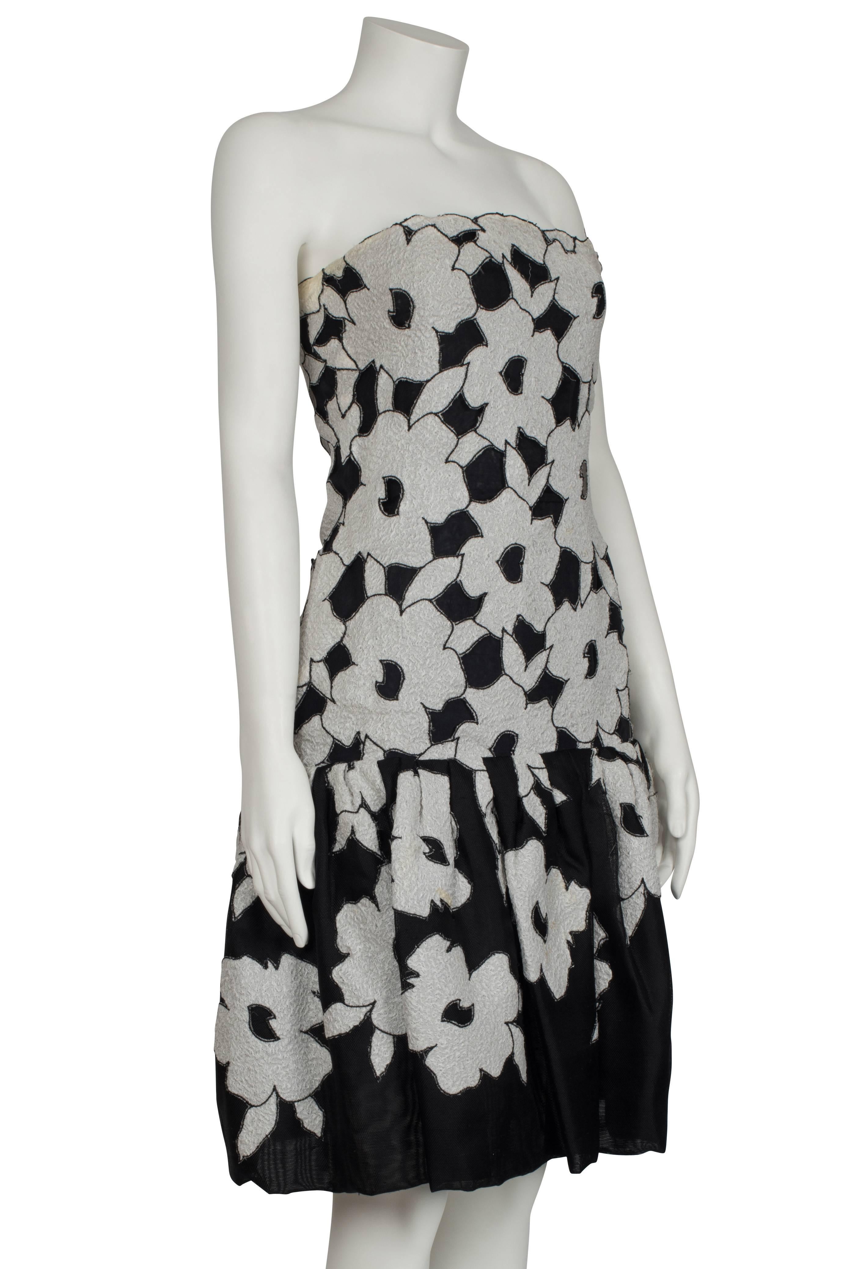 An elegant Christian Dior couture monochrome silk bandeau cocktail dress from the Spring/Summer 1983 collection. The strapless structured bodice is constructed from black silk with an overlay of textured white silk appliqued flowers. The dress