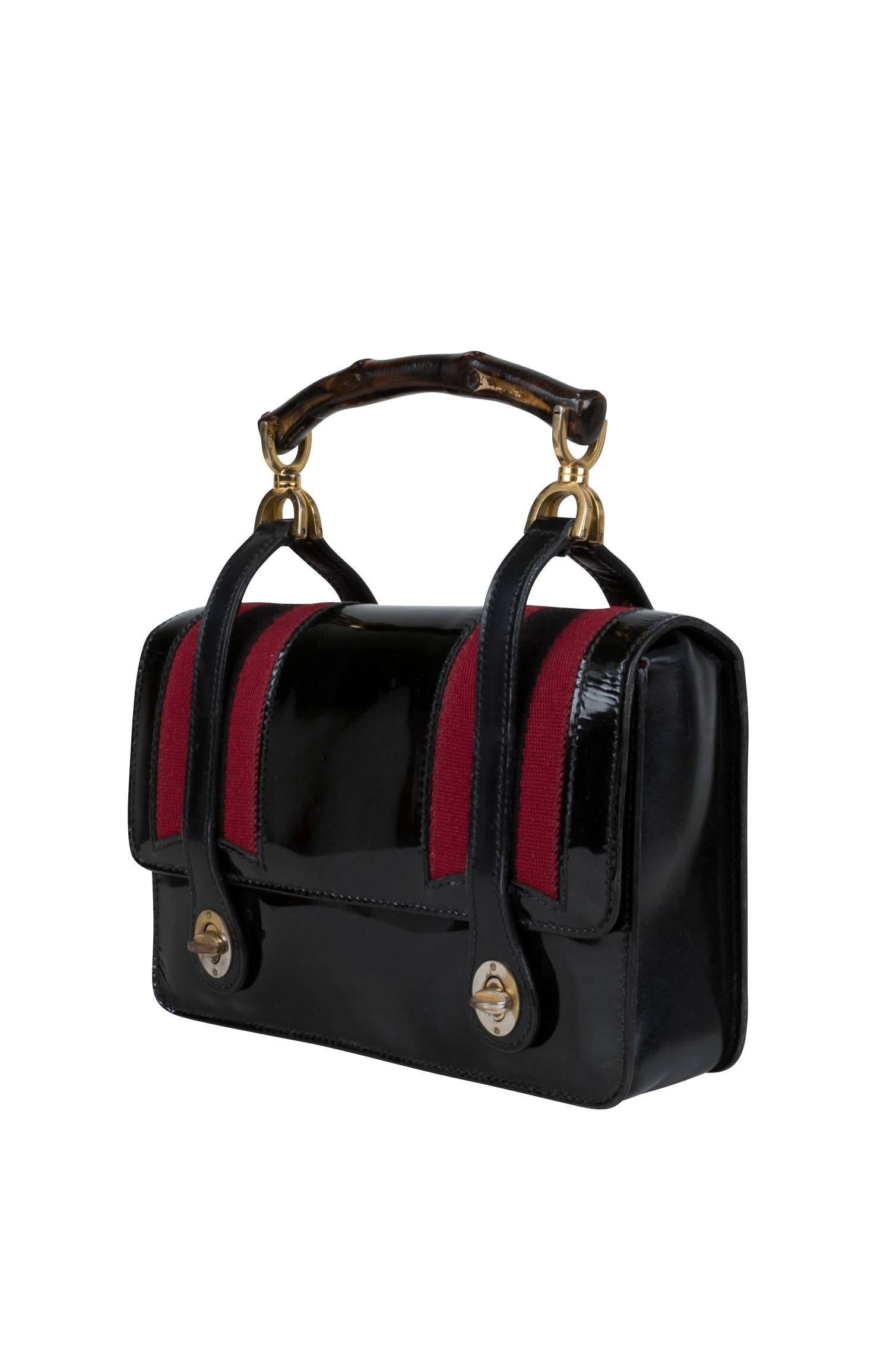 A 1960's patent leather Gucci handbag. This elegant mini lunch box bag features the label’s signature woven alternating stripes in black and red and a signature bamboo wood handle. A flap opening features two matte black leather teardrop straps with