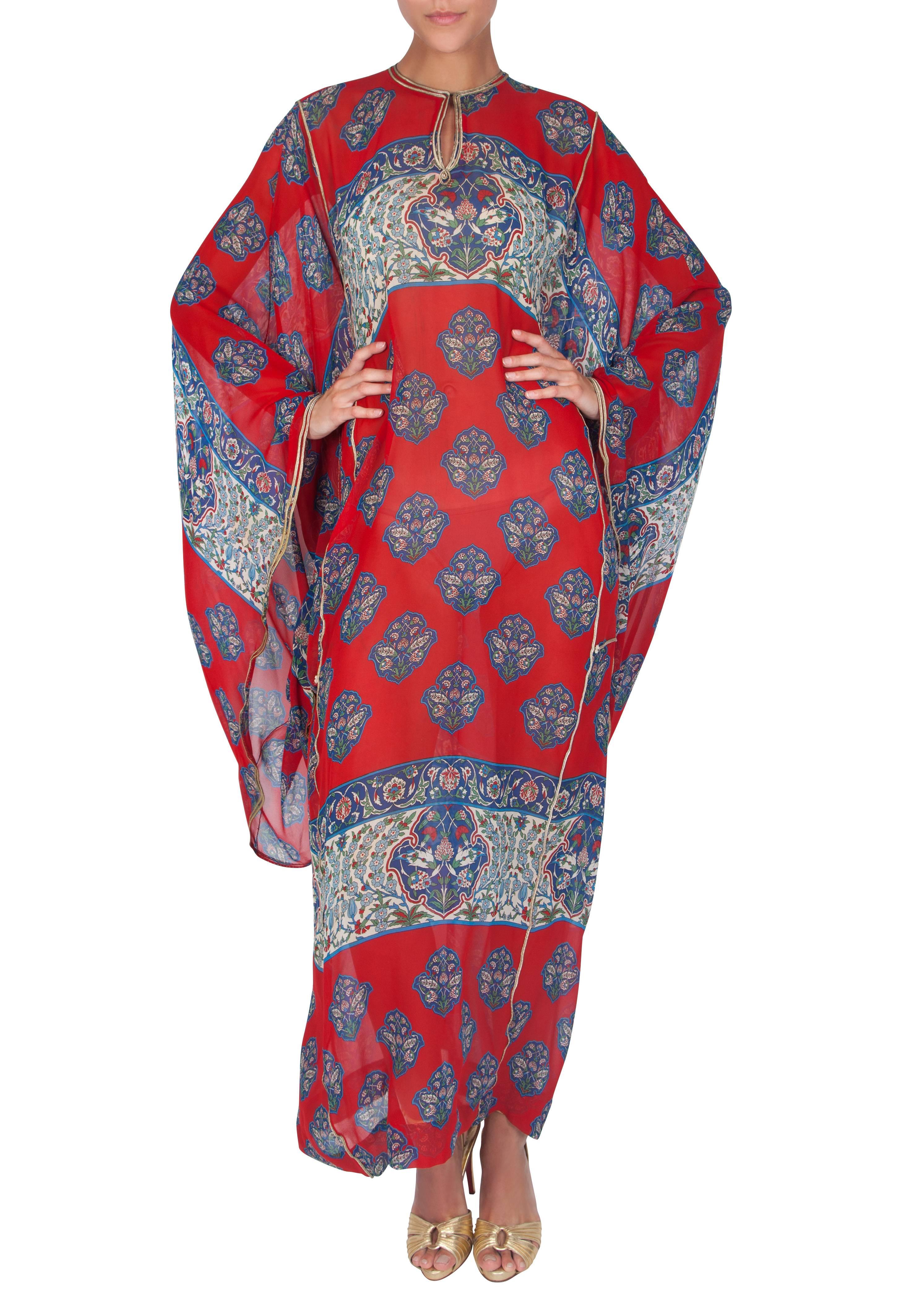 A rare red silk chiffon caftan with a blue and white floral pattern by London boutique Arabesque. The full-length flowing caftan features a metallic gold braid trim and full-length billowing batwing sleeves. An adjustable slit neckline can either be