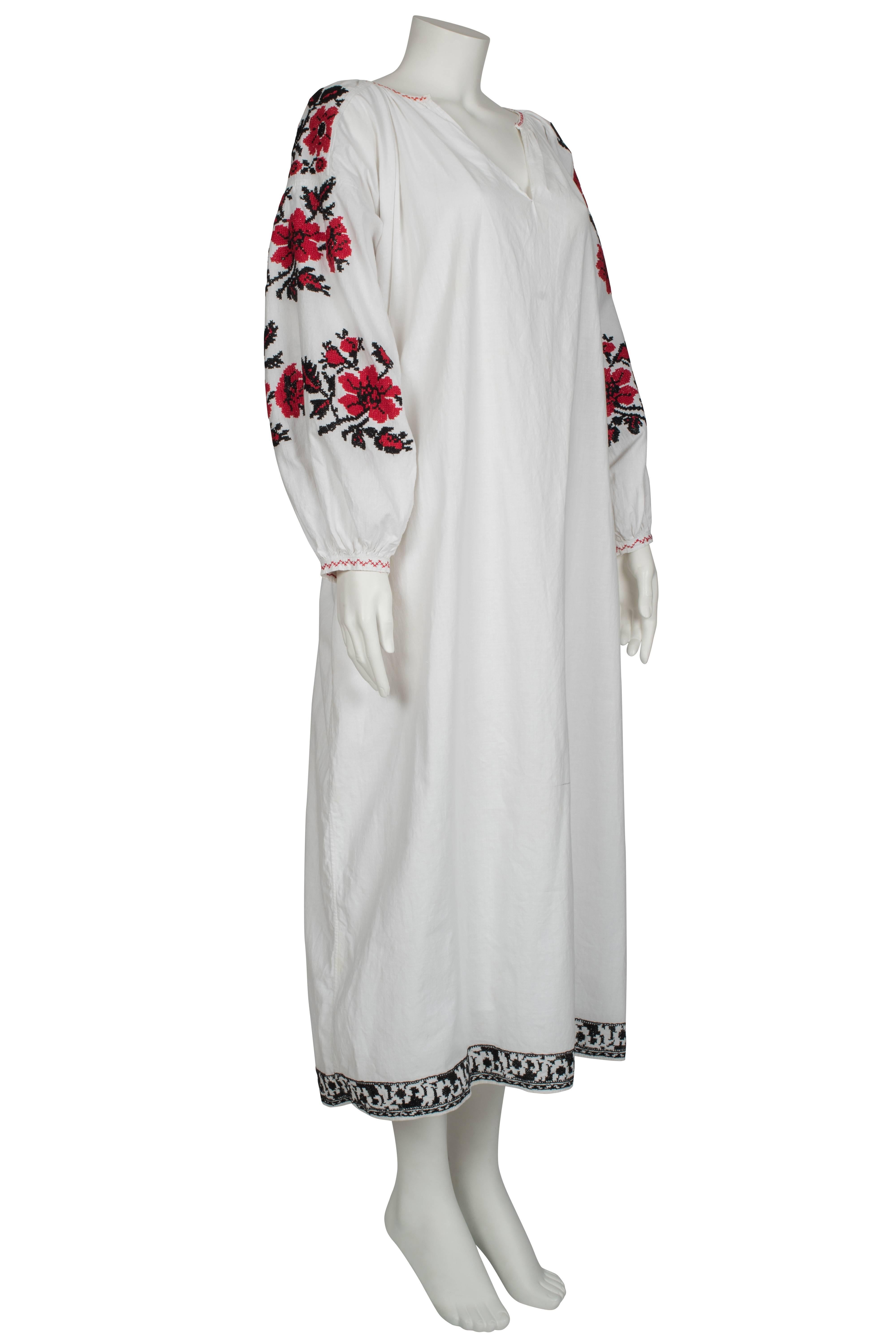 A 1970's Vyshyvanka cotton dress, hand embroidered according to Ukrainian Folk tradition, featuring a red and black cross-stitched floral pattern on both sleeves. A relaxed fit throughout, the dress has oversized sleeves and a discrete v on the