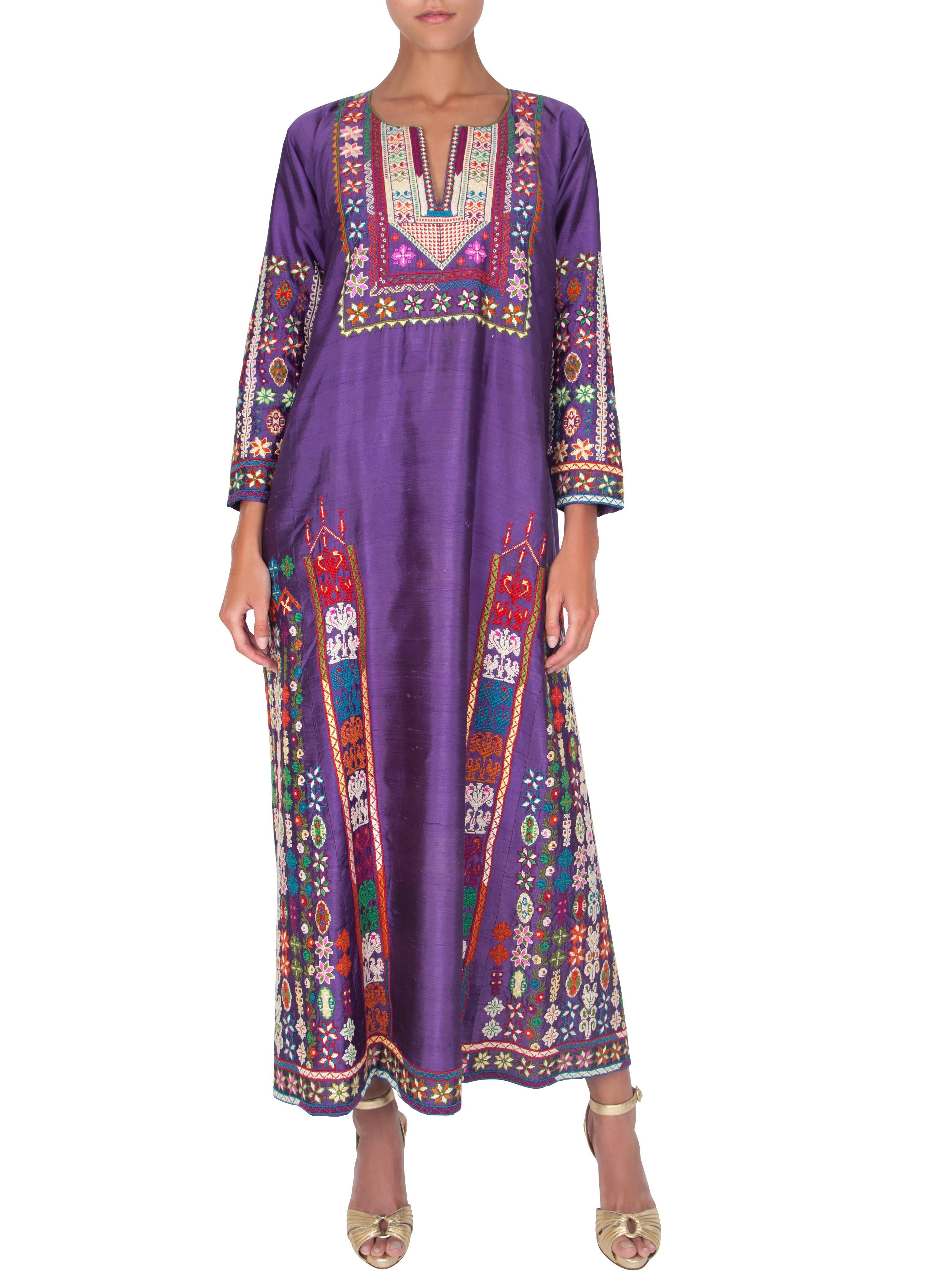 A vibrant amethyst silk caftan with multicoloured embroidery hand-embroidered in Palestine using traditional craft methods from the 1960s/70s. The label specifies ‘Embroidered by Palestinian Women according to Traditional designs.’ The full length
