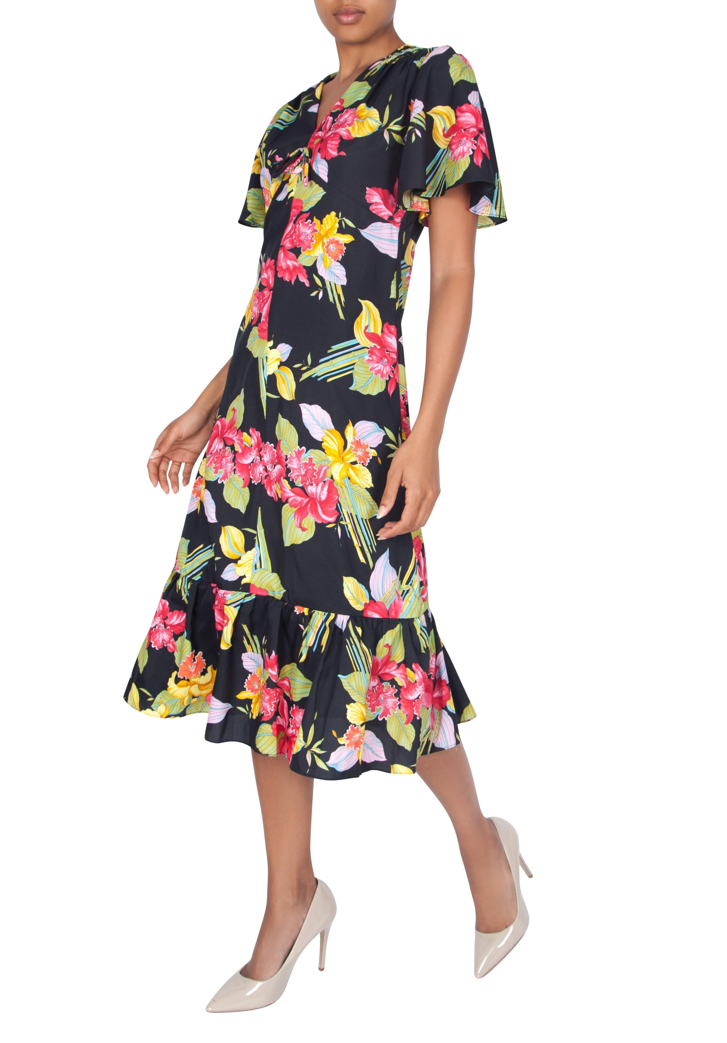 A feminine and versatile 1970's black dress with pink and yellow floral pattern, featuring a slight ruching on the shoulders from which flared sleeves come forming a capelet-like shape. The empire line accommodates the bust in a semi-circular cut