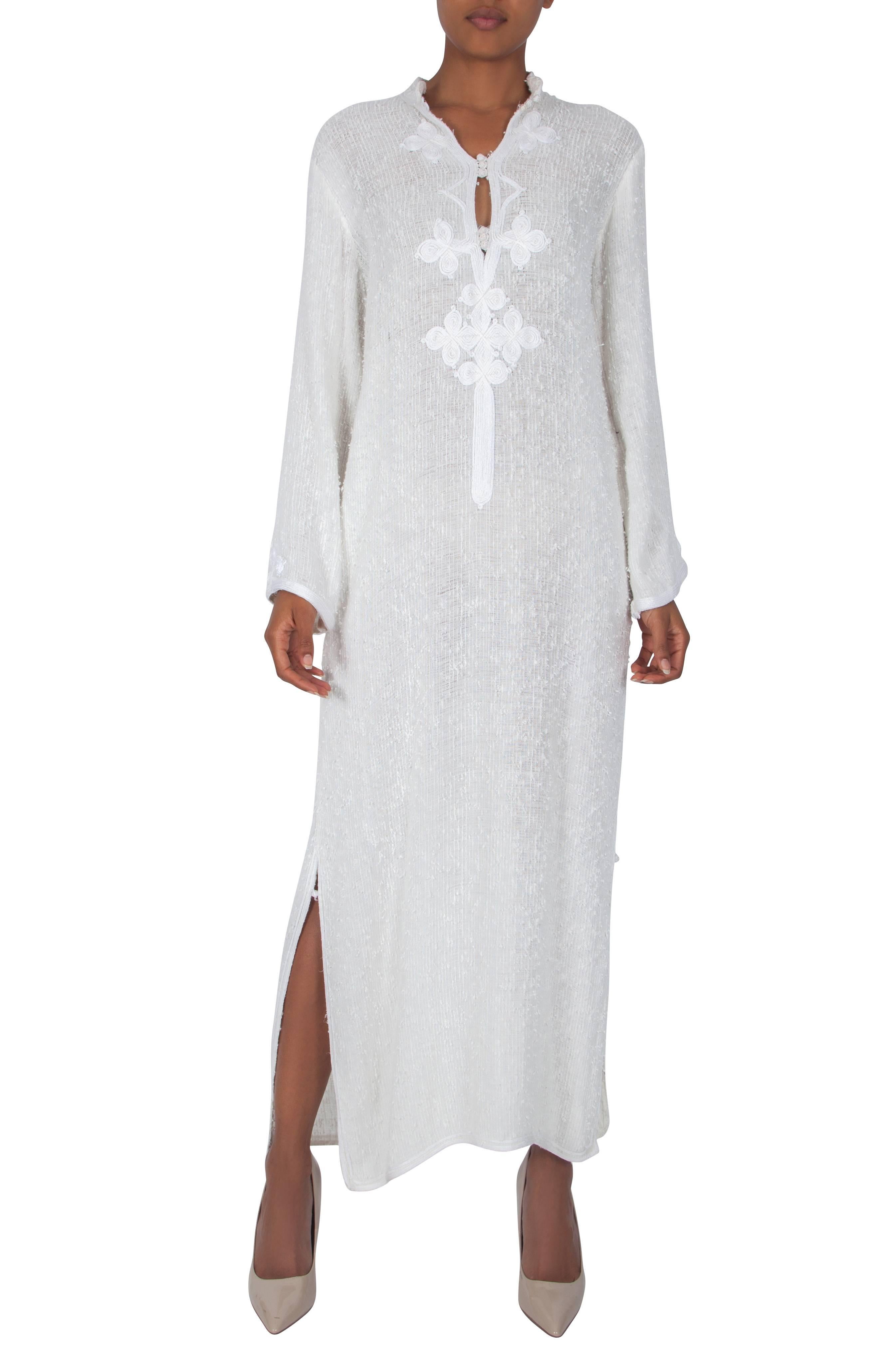 An ivory cotton maxi-length tunic by London-based couturier Harald. The open-weave textured tunic features a high collar made of pearlised white silky soutache embroidery and a slit neckline which can be fastened with three sets of three pearlised