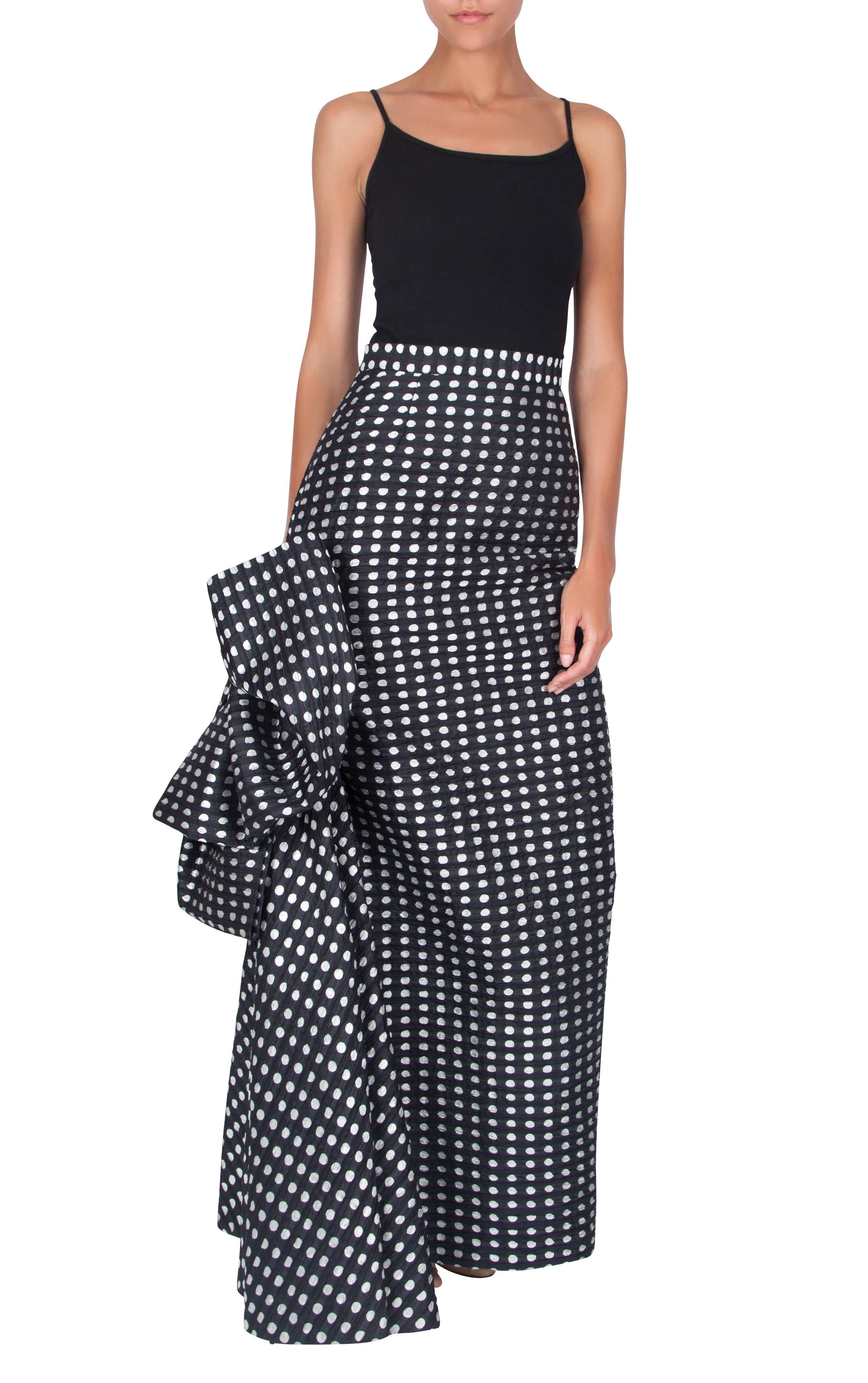 A statement 1980's Yves Saint Laurent maxi skirt, made from a textured silk fabric in a polka dot pattern. The focal point of the skirt is the dramatic oversized bow on the right side, which contrasts with the otherwise simple and straight design of