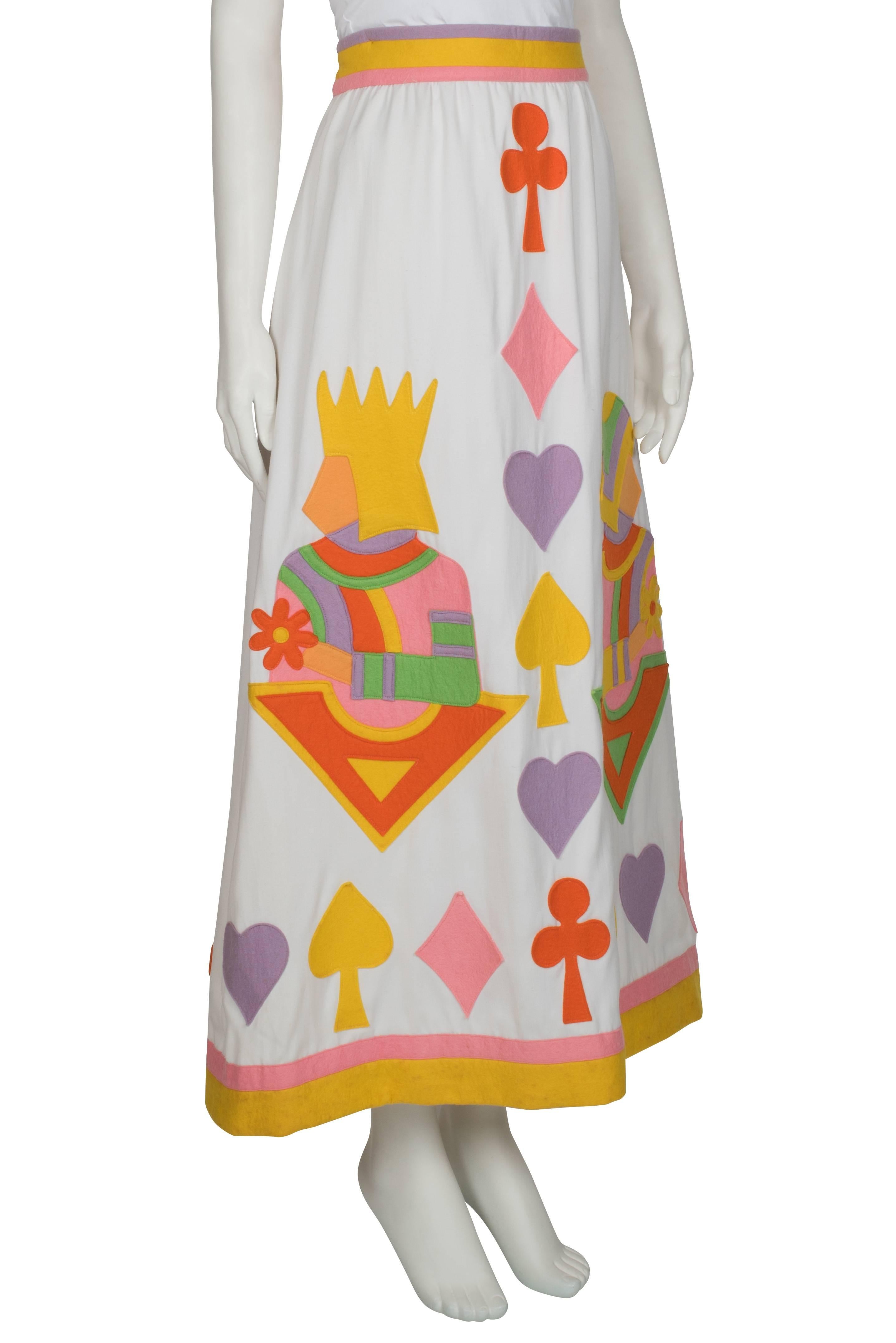 A 1970's skirt by Rizkallah for Malcolm Starr. Made from white cotton twill, this skirt features felt appliqués in the shape of card suits and felt bands on the waistline and hem. Additional features are two deep pockets on either side. The skirt