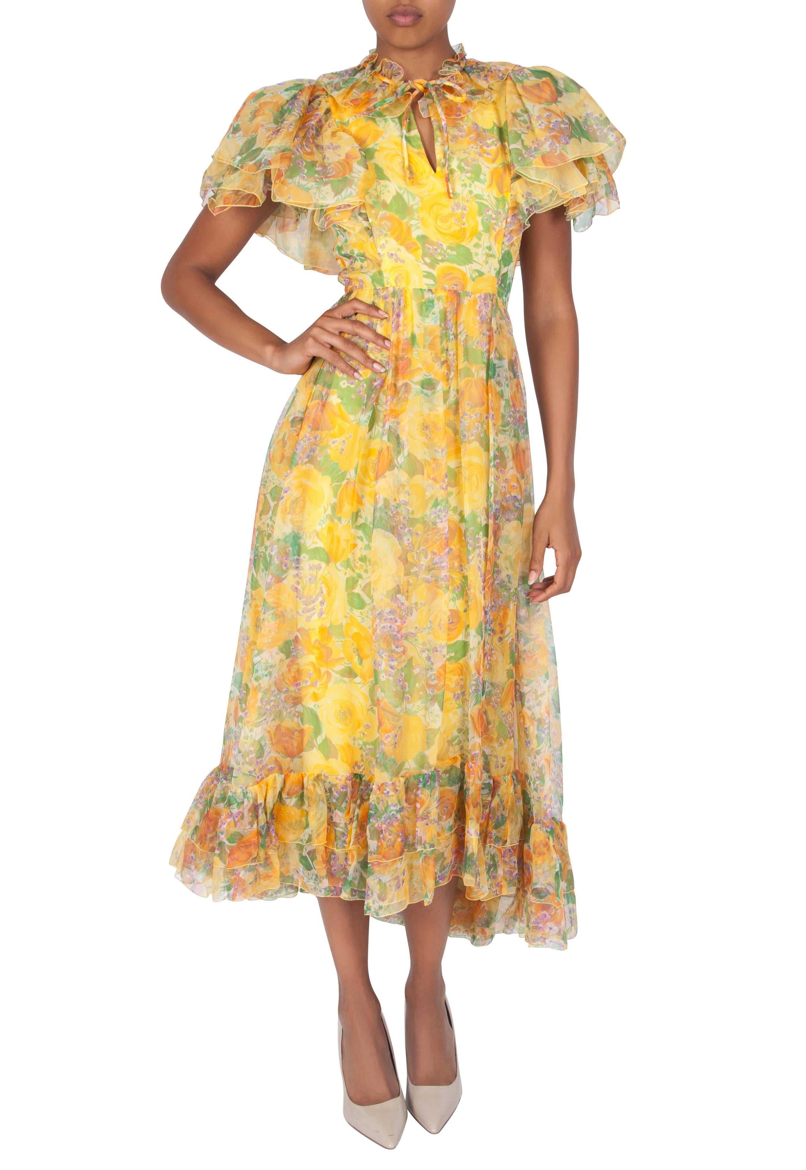 A 1970s yellow floral silk organza dress by London couturier Harald. The full-length dress is fitted to the waist and features a V neckline, ruffled neckline trim and a necktie that allows the dress to be closed at the neckline, forming a keyhole