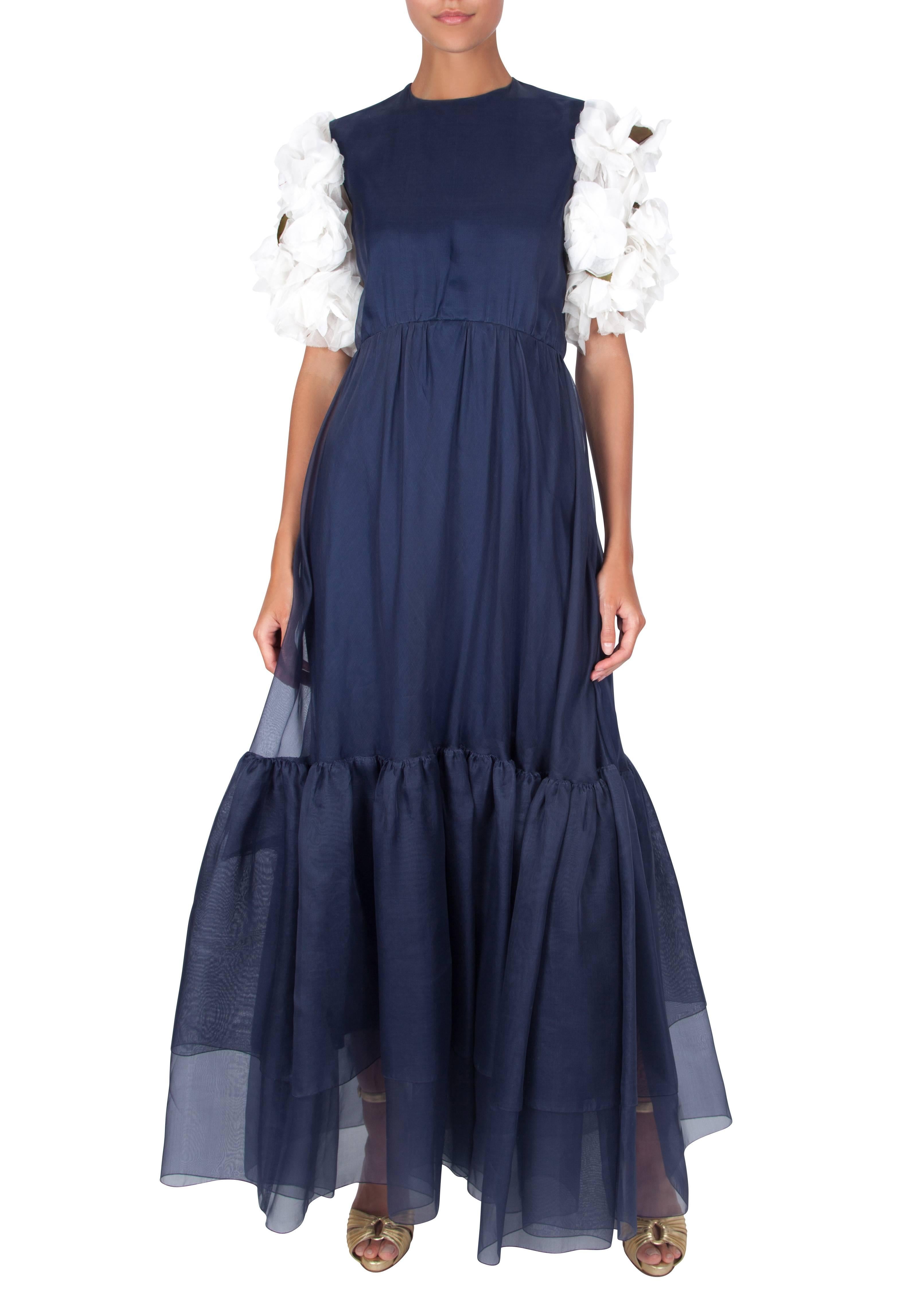 A navy blue silk organza dress with puff sleeves featuring from white appliqued flowers by London couturier Harald. The full-length dress is constructed from a dark blue polyester jersey underskirt with a layer of navy blue sheer silk organza over