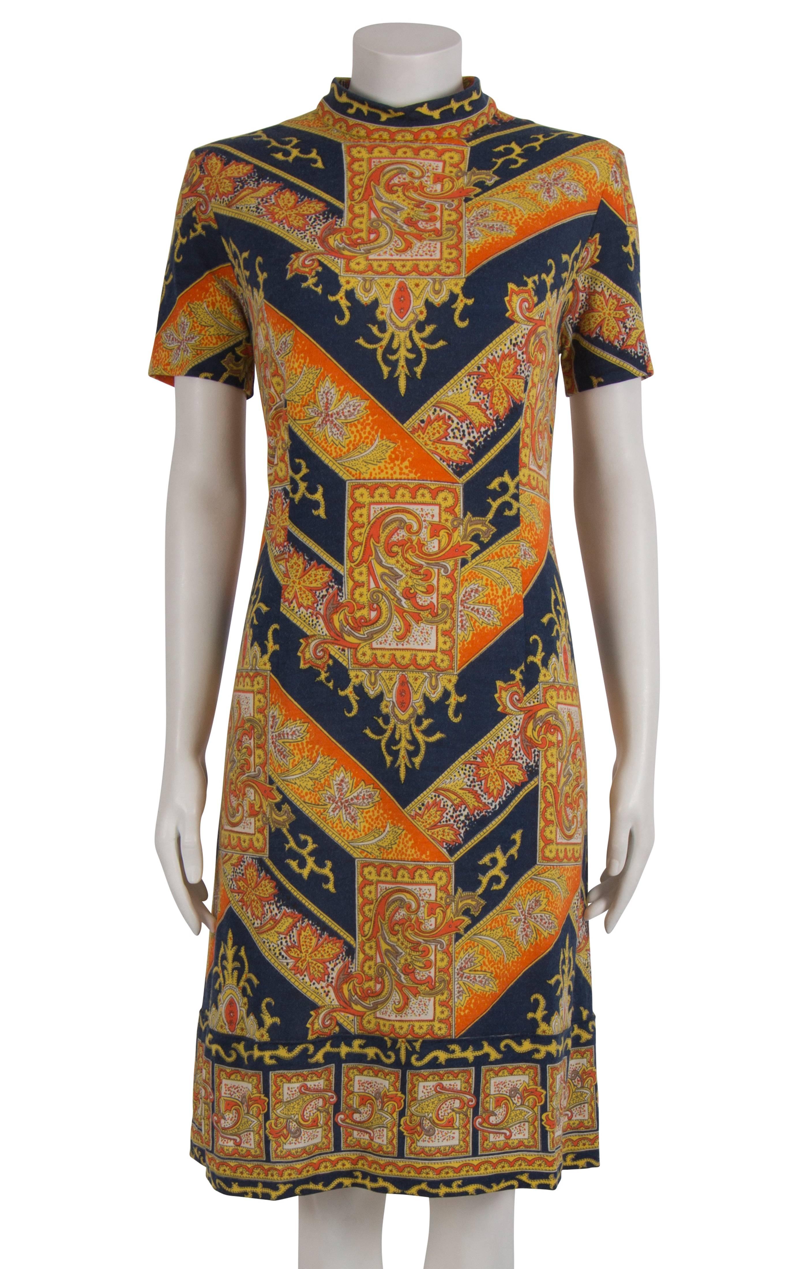 1960's Austrian made wool and rayon dress, featuring a heraldic motif in orange, yellow and navy. The dress is a shift shape, with a square printed insert on the hem giving the illusion of a pleating. The dress is fully lined in ivory acetate, and