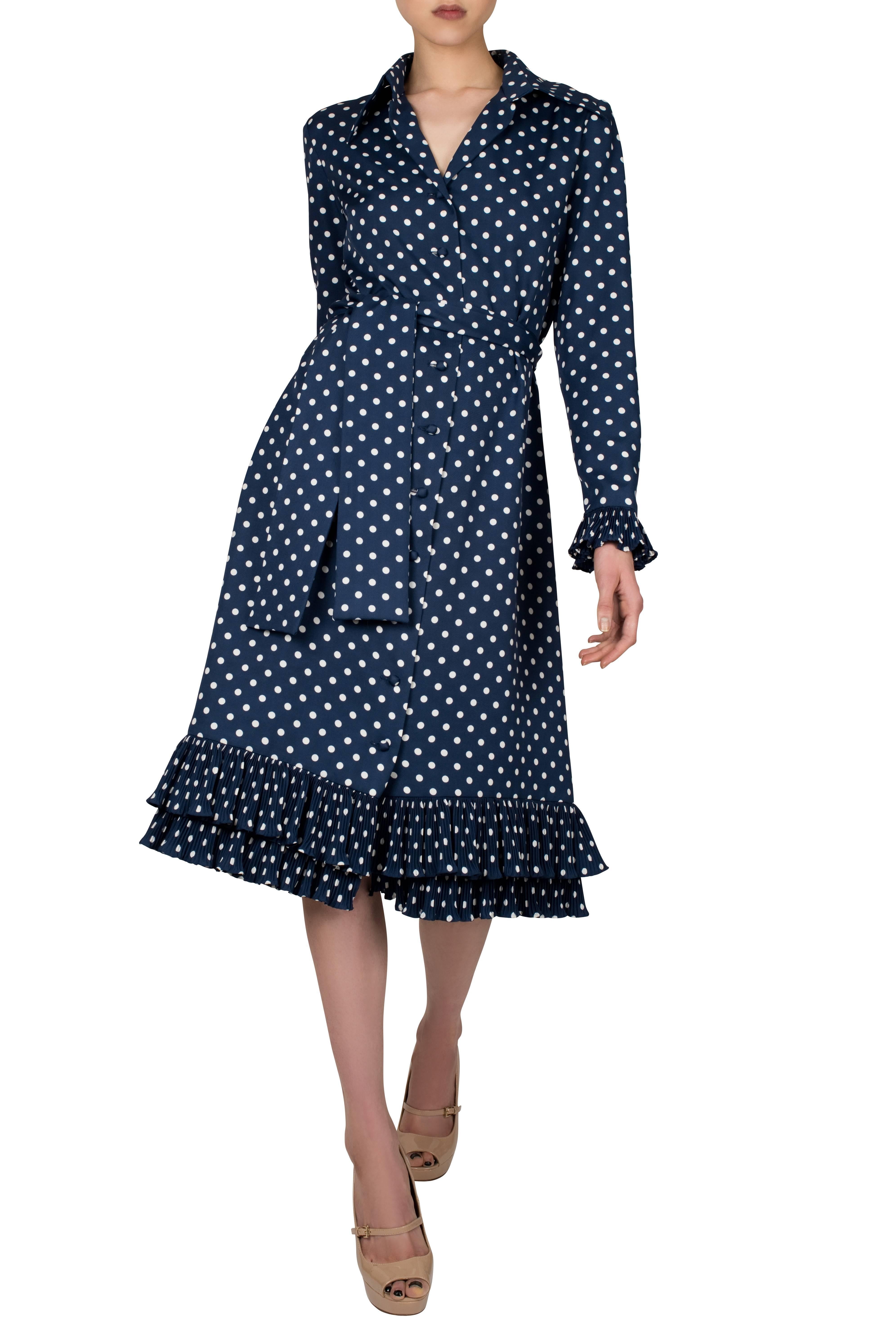 Beautiful 1970's Victor Costa shirt dress. Made from a soft synthetic fabric in navy blue with white polka dots, the dress is buttoned down in the front with micro pleats embellishing the cuffs and hem. An additional feature to the dress is a wide