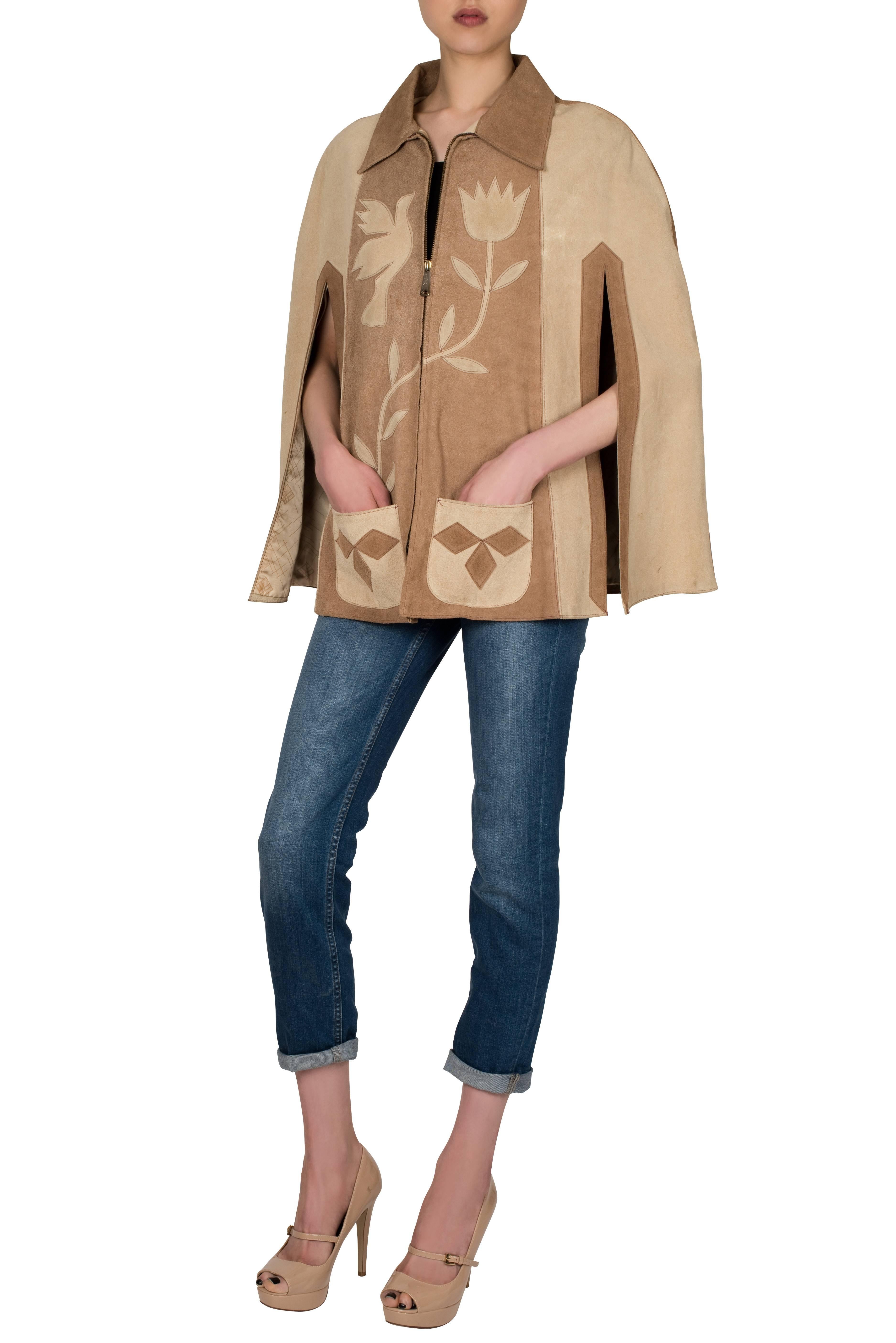 A Mexican-made 1970's suede poncho cape in tan and beige hues. The cape features contrasting appliqués in traditional Mexican designs. Fully lined in a polyester satin, the jacket zips up at the centre front. Excellent vintage condition, no tears