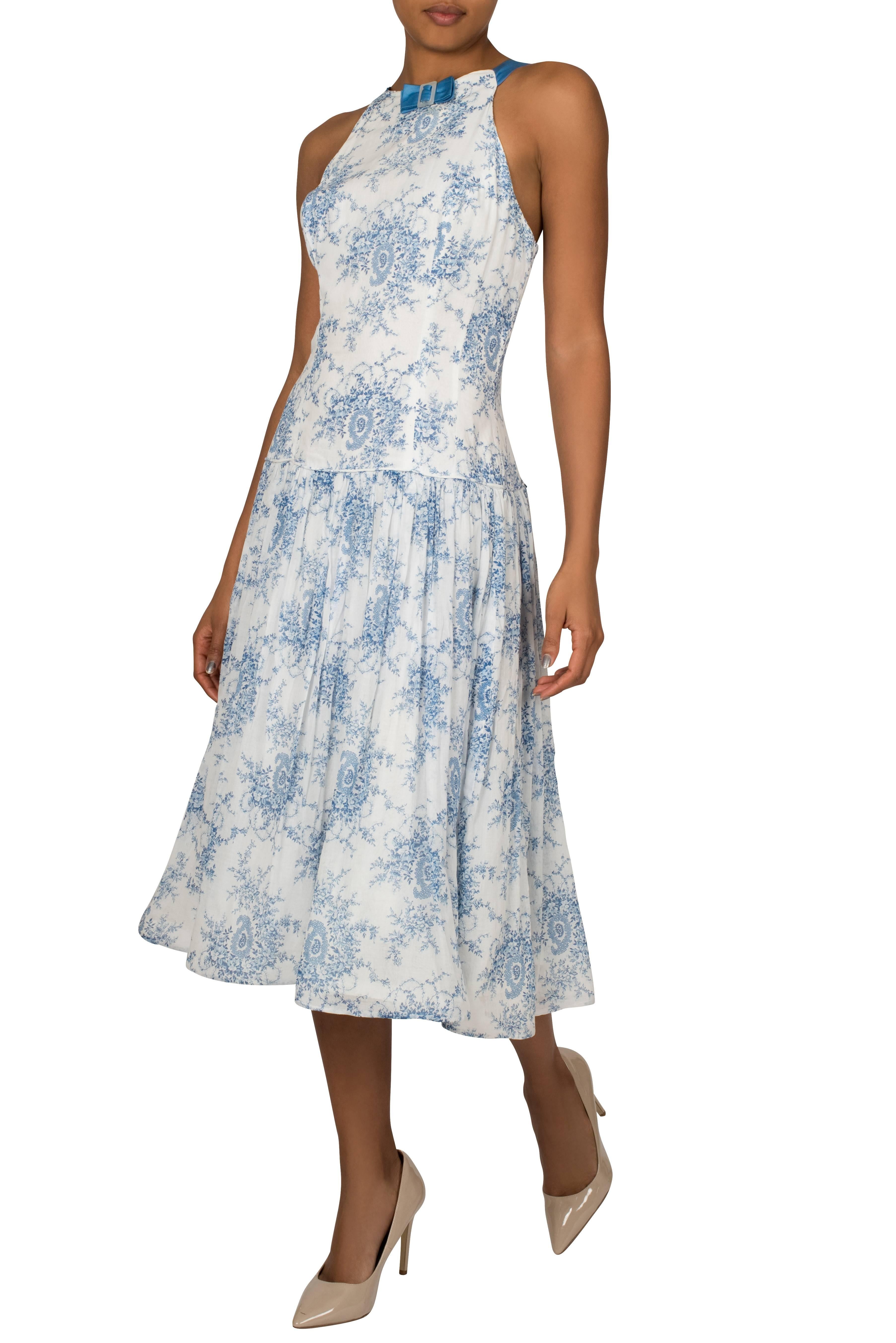 This beautiful late 1940's dress features a floral and paisley print in dutch blue on soft white lightweight woven cotton. The high neckline is detailed with a simple blue bow and the shoulder straps, also in blue reveal a low gradually scooping
