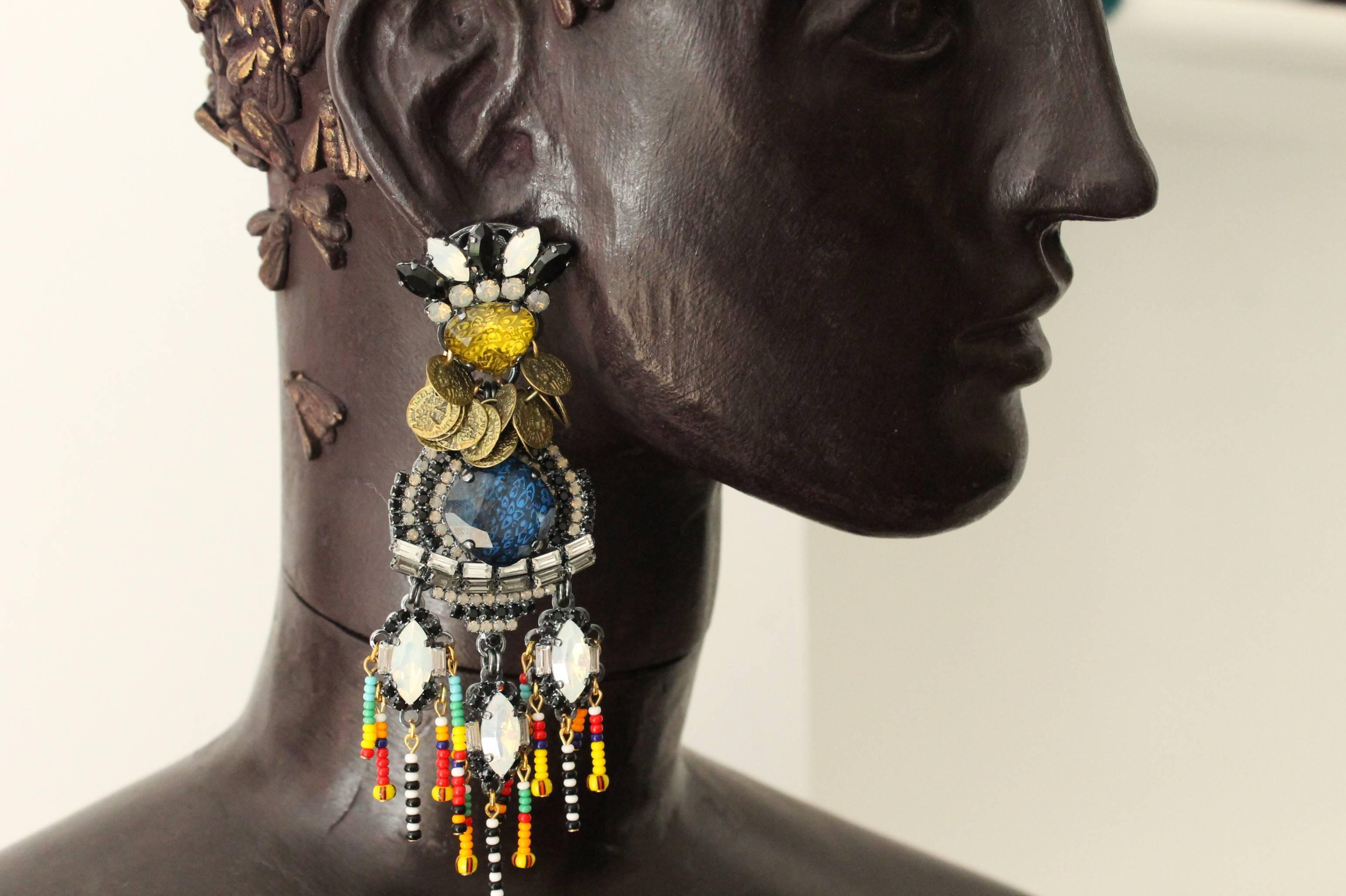 Stunningly beautiful statement drop earrings, lavishly embellished with hand-enamelled white, yellow, blue, black and clear Swarovski crystals; brass coins and rainbow-coloured seed beads.

Handmade for the past 25 years by Vicki’s small team of