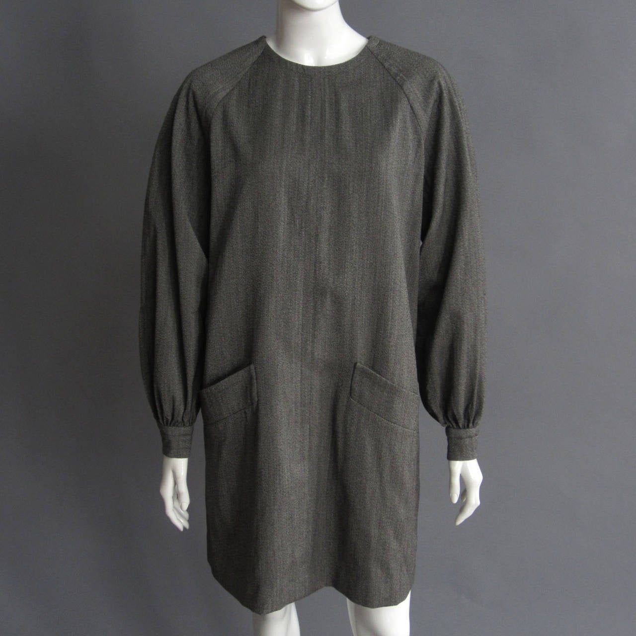 Grey wool smock dress that is the epitome of Parisian chic. The raglan sleeves are voluminous, cinching at the wrist with a seamed cuff and single button closure. Front, hip pockets are trimmed in matching grew wool with seam detailing. Fully lined.