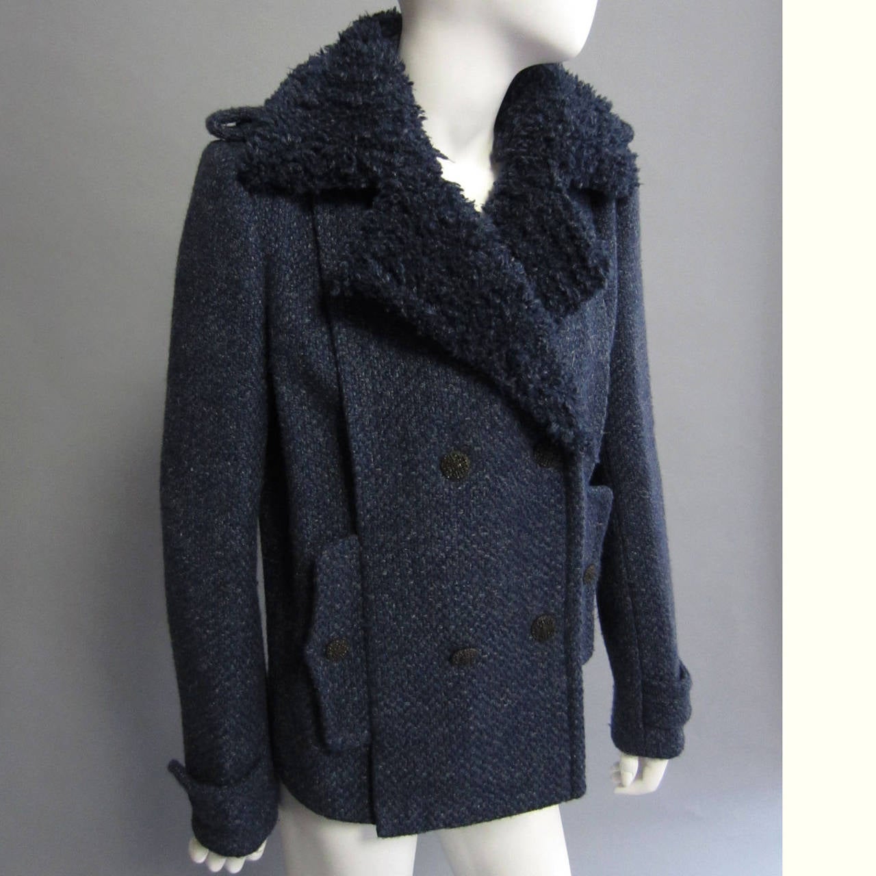 Authentic CHANEL, this coat is made of a blue and navy tweed. The richness of the color is accentuated on the collar; the wool is gathered and sheared to create a faux fur like trim. The double breasted closure showcases the intricate, CHANEL logo