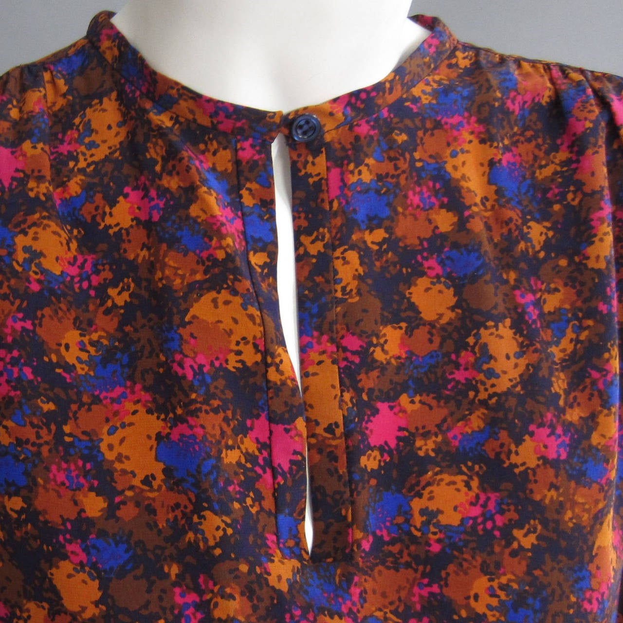 The gorgeous print silk of this YSL blouse features rich colors, splashed together creating an abstract, paintbrush effect. The front features a keyhole at the center of the neck. It is secured closed by a single button, or could be left open. There