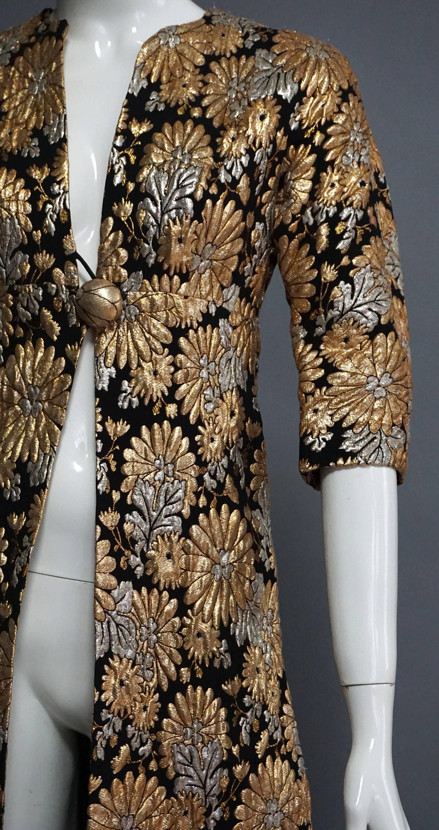 This coat is all about the fabric. The golf and silver lame threads create a floral pattern that is simply stunning. The mixed metallics are woven on a black backdrop, making them pop even more. The coat is fitted at the waist. At the front center