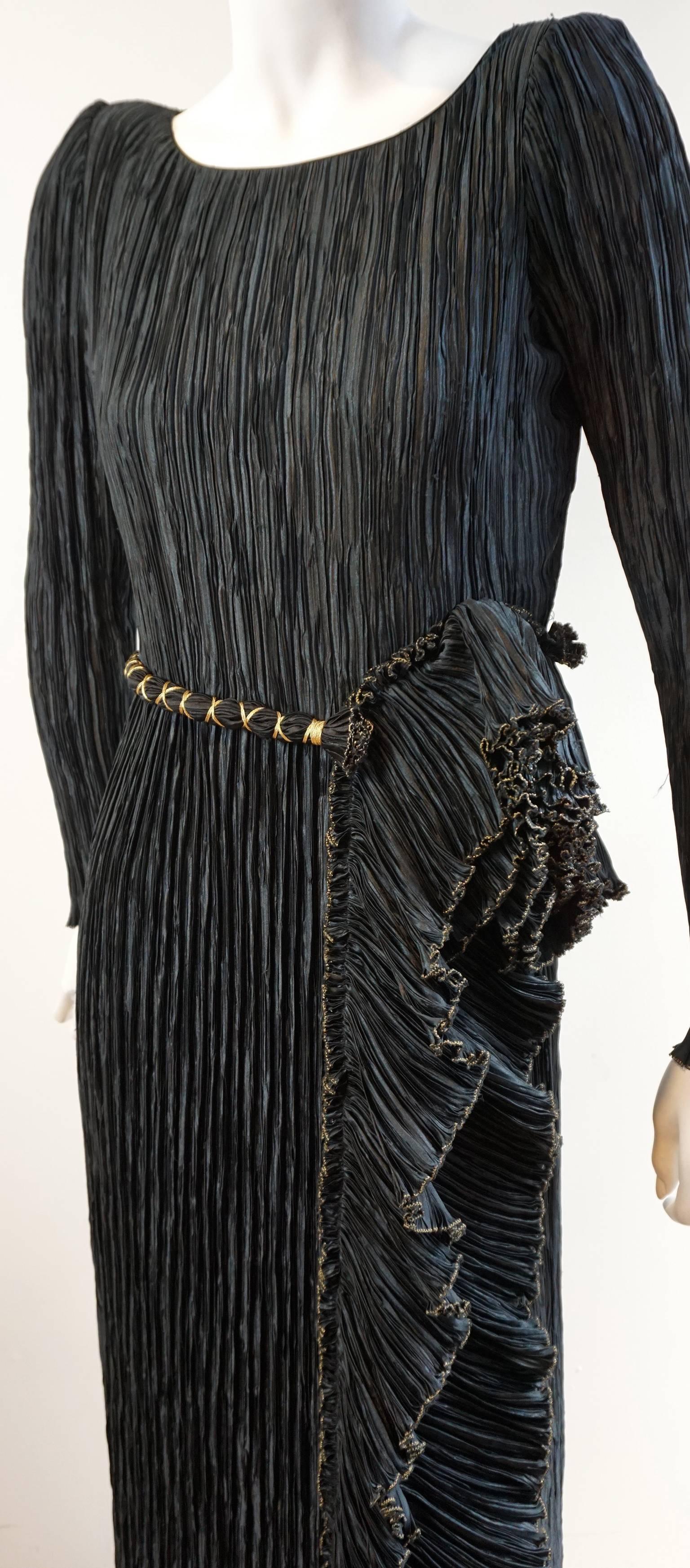 Comprised of the quintessential McFadden pleating, this gown features long sleeves with slight padding at the shoulders. The waist is highlighted with a black and gold rope belt with frayed edge. It is attached along the front and secured with a