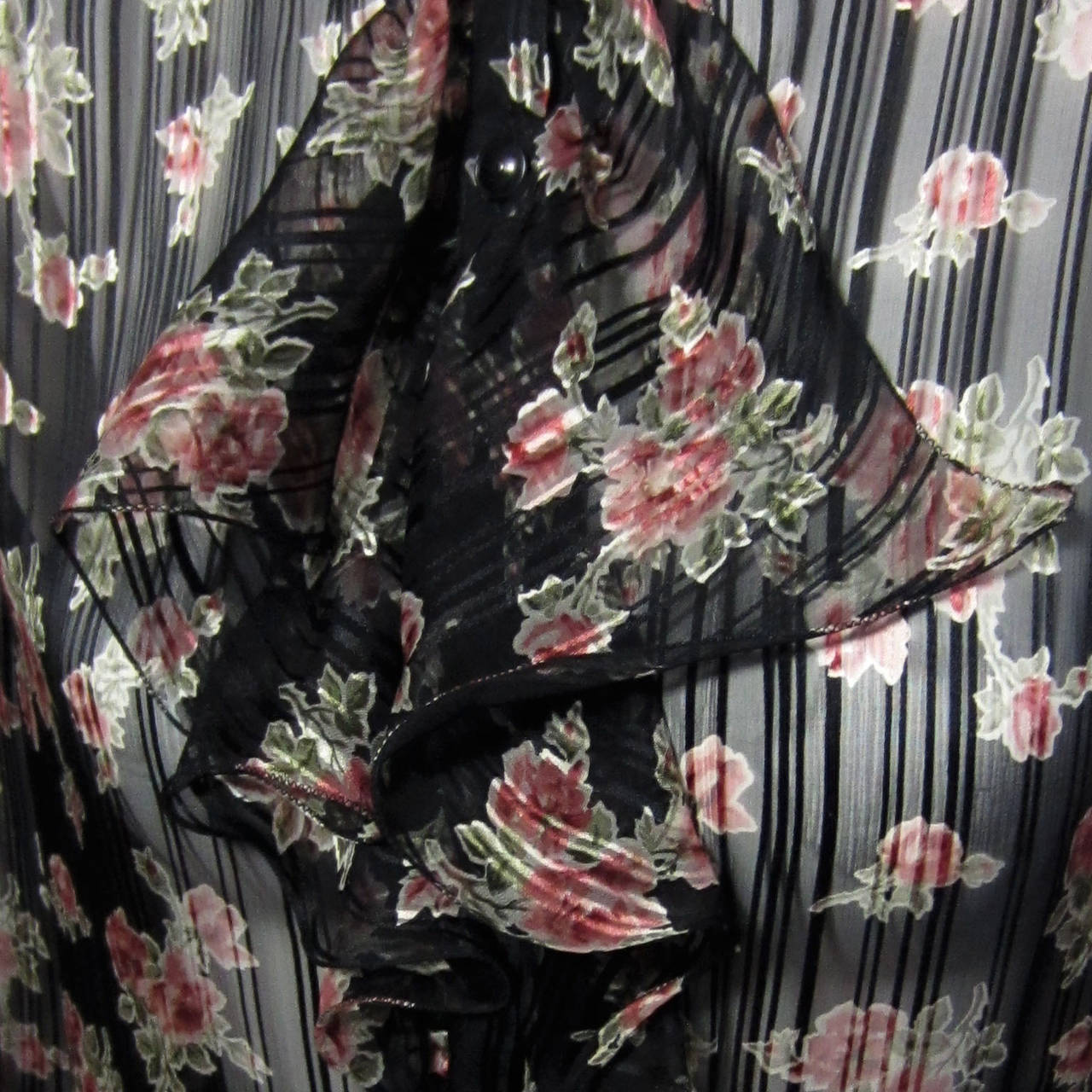 The sheer, black silk of this UNGARO blouse features a staggered, stripe design. Layered on top, there is a detailed rose print covering the entire blouse. The front opening features a tiered, ruffle detail originating at the neck. There is a small,