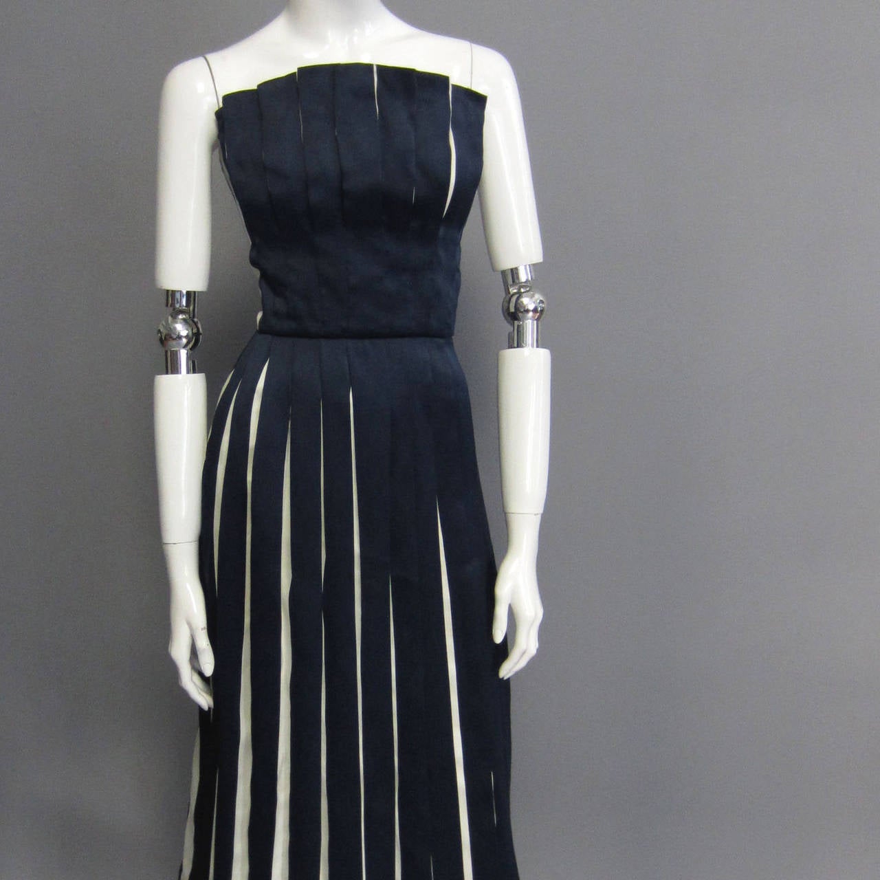 This Victor Costa silk taffeta creation features navy and white pleats throughout the entire dress. The skirt is fully pleated with the contrasting colors. The pleats are layered on the bodice to create a fan like effect across the top. The back