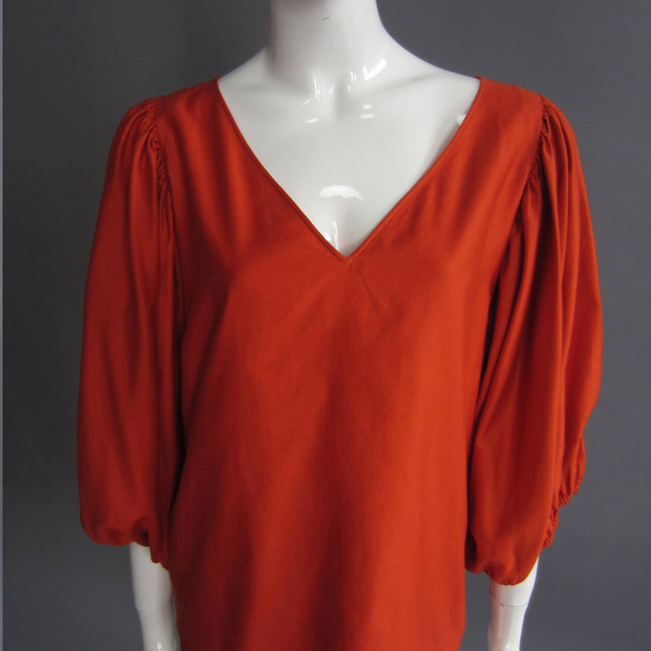 Simple, chic and YSL. This blouse is a beautiful shade of orange. The silk/cotton blend adds a sheen that gives the color even more dimension. The 3/4 sleeves are voluminous. The feature elastic around the end; the elastic is worn so the bottom of