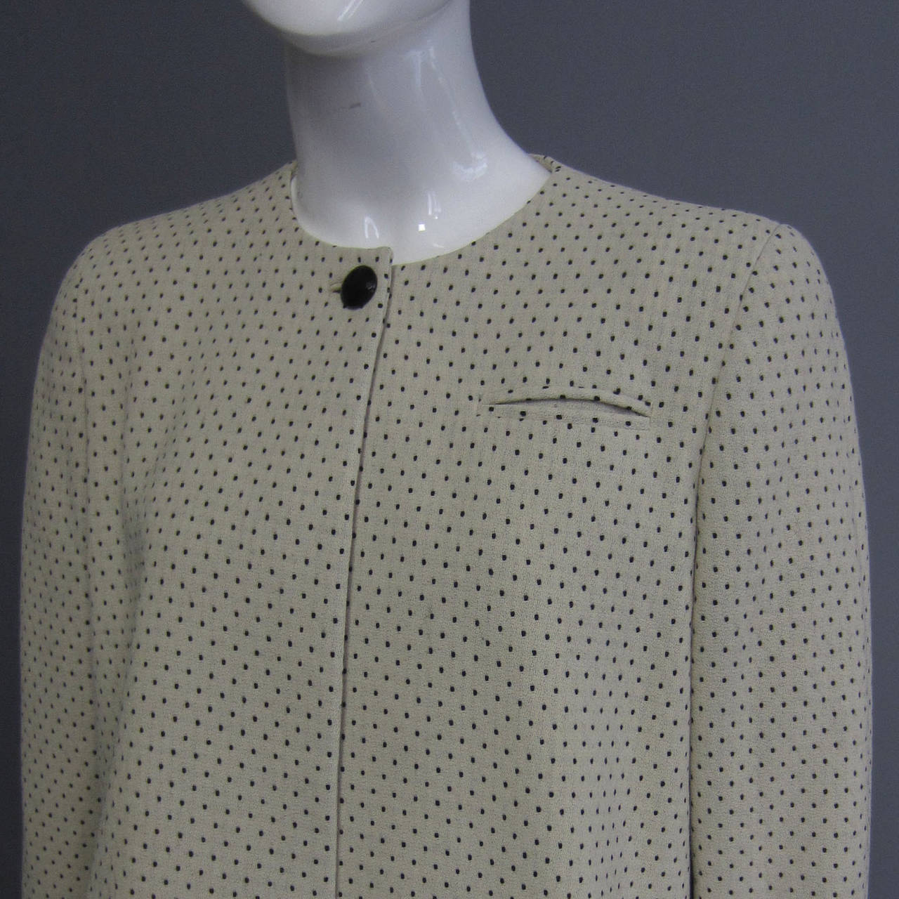 A tiny, black polka dot is set against a creme wool background. The print is faint, but adds texture. The jacket is cropped, hitting at the waist. The jacket is slightly longer in the back, which also features extra fabric to create a swing effect.