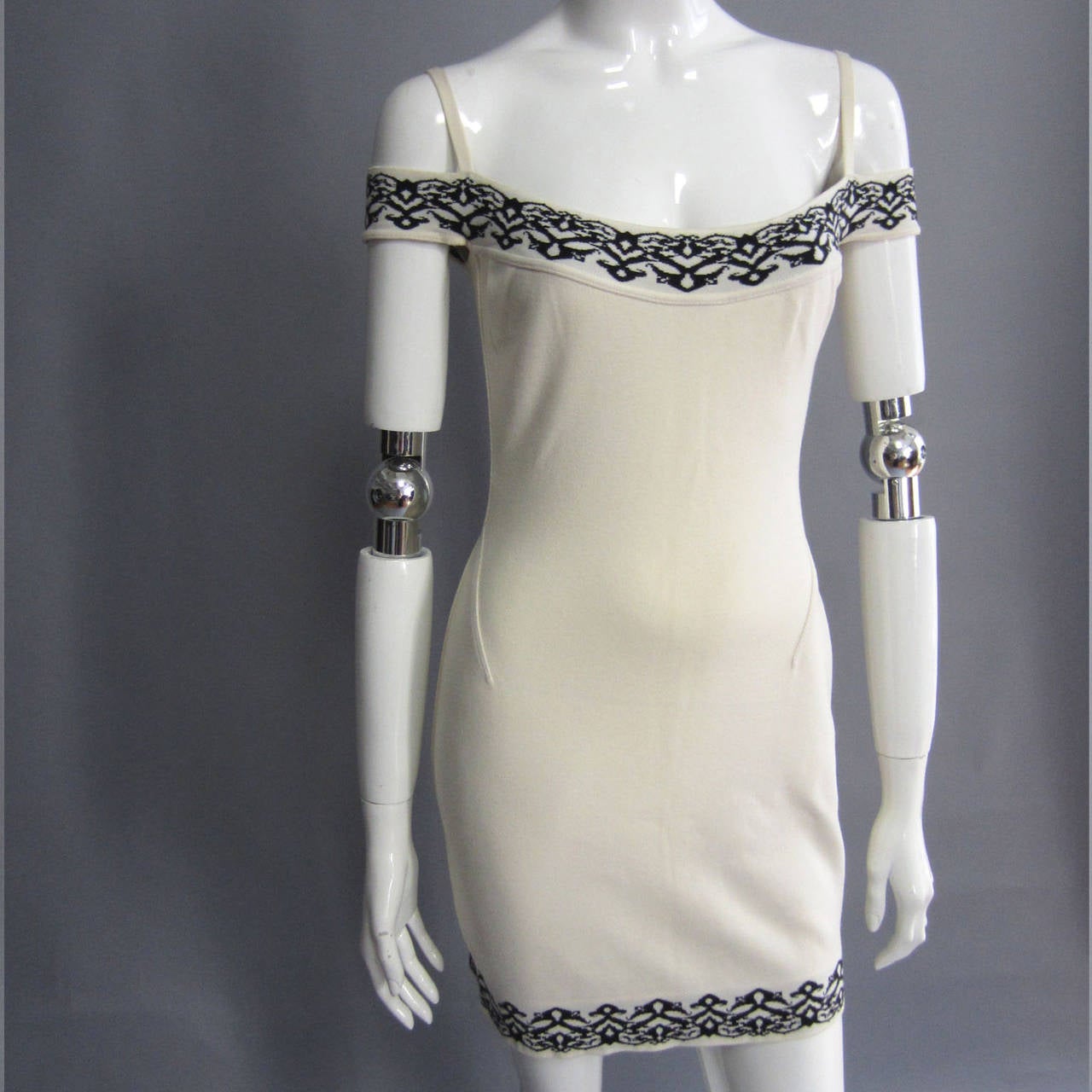 Classic ALAIA. This dress is off white. The mini dress features seam details throughout that accent the curves of the body. The black, graphic print trim is featured around the hem, bodice, and arms. The dress is designed with a thin, off white