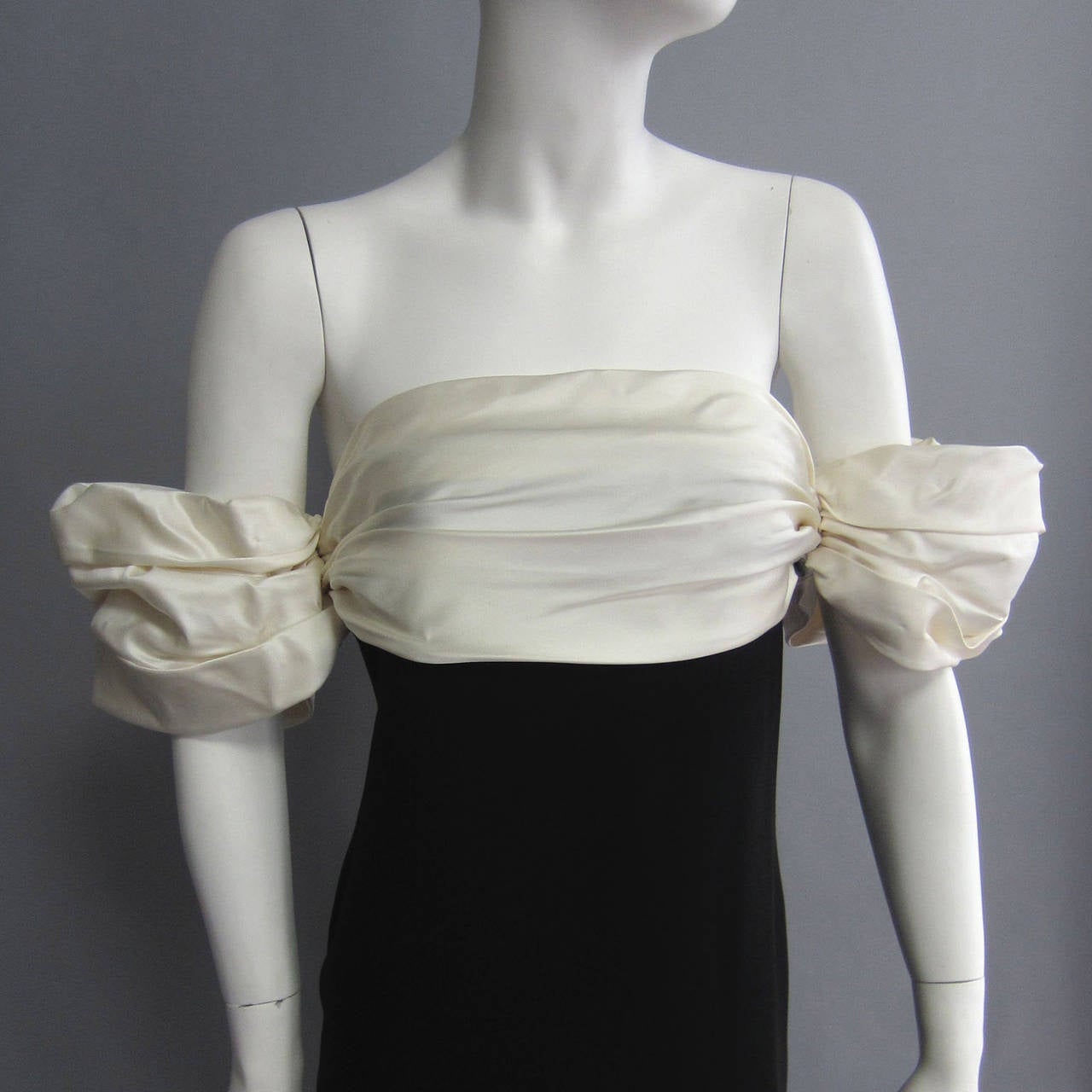 A sophisticated gown from designer BILL BLASS, this dress is sticking and yet simple. The body is made of black wool. THe bodice is trimmed in an off white satin; the fabric is ruched to create a cumberbunn look. The same fabric and ruching effect
