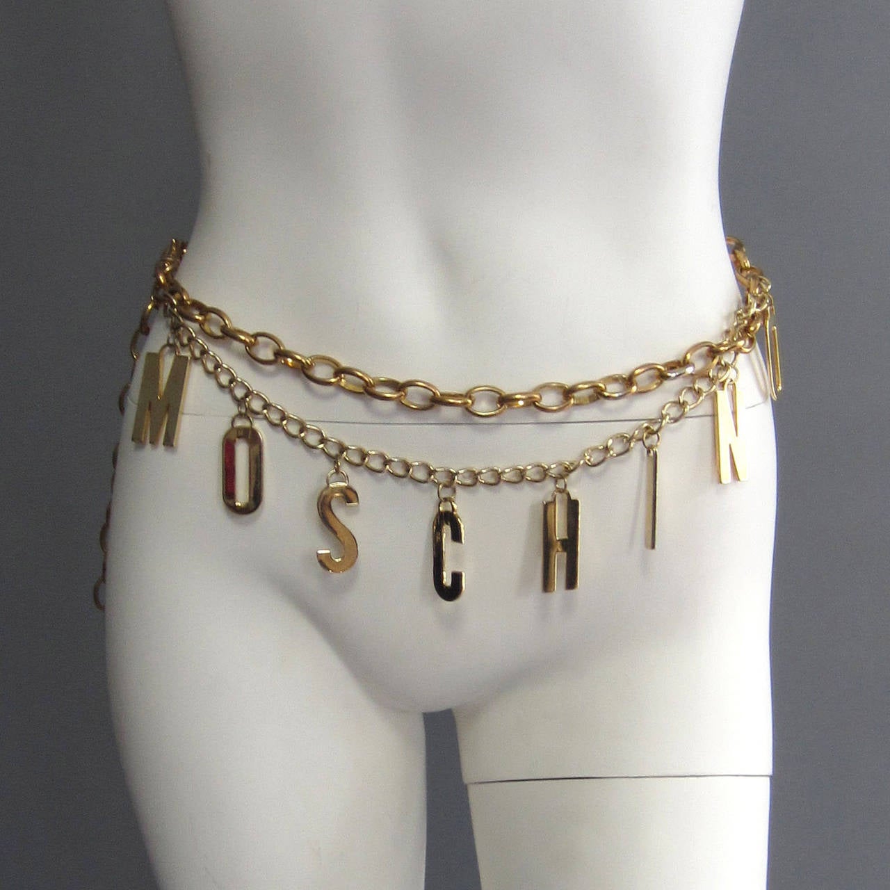 M O S C H I N O  spells MOSCHINO! This adjustable chain belt features these letters, each hanging from an small chain that swags below the main, thicker chain. With a hook closure, this belt can be adjusted to a wide range of sizes by simply