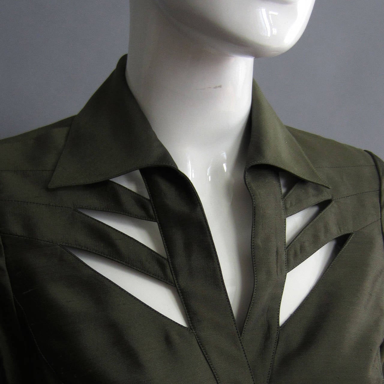 The silk fabric gives the rich, army green color a beautiful sheen. The dress is fitted with snap closures up the front center. The collar detail is accented by a series of cutouts on either side. The cutout also highlight the neckline and overall