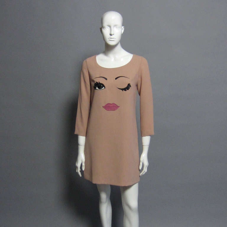 A sophisticated, blush colored shirt dress with the quintessential whimsical MOSCHINO detail. The front embroidery creates a face, with a lovely, lashed eye winking. A fun dress for day or night, MOSCHINO is never afraid to bring a little humor into
