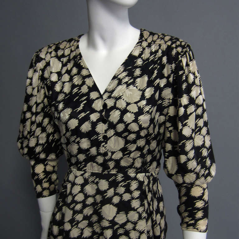 Creme on Black silk painterly print. Slight puff sleeve narrows  with single button and loop closure at wrist. Matching button and loop closures on front chest. The V neckline is accented with slight pleating on the shoulders. Pleating from waist