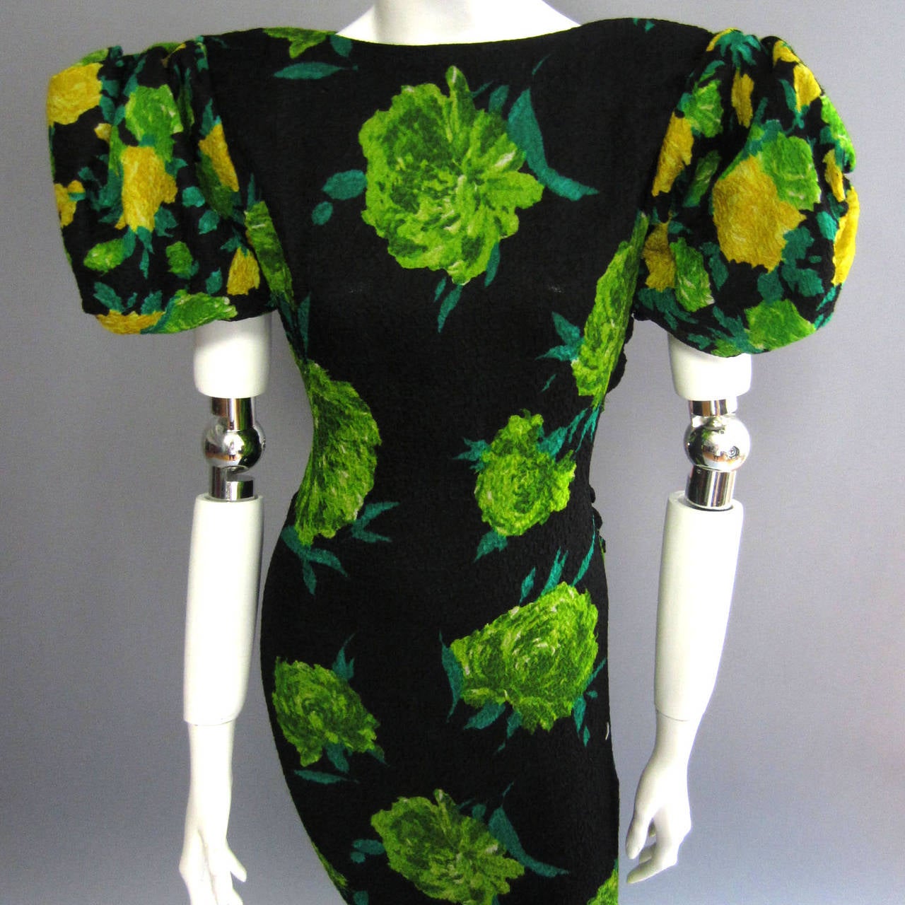 This JAMES GALANOS gown features a gorgeous crinkled silk fabric that is covered in a bold, kelly green floral print accented with yellow roses. The fabric  has a slight amount of stretch, so it clings to the body. This is particularly true along