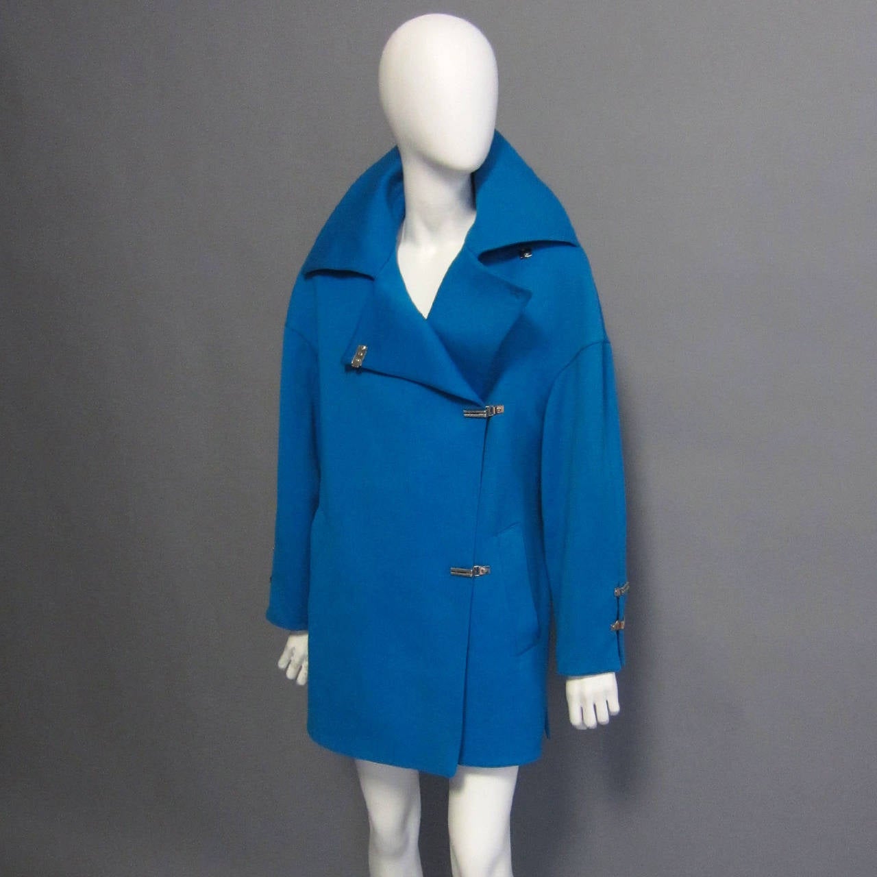 This MONTANA coat is made of a bright, teal wool. The bold color is striking, but also highlights the design details of this beautiful coat. The asymmetrical closure is secured by a series of silver, metal toggles. This hardware is repeated on the