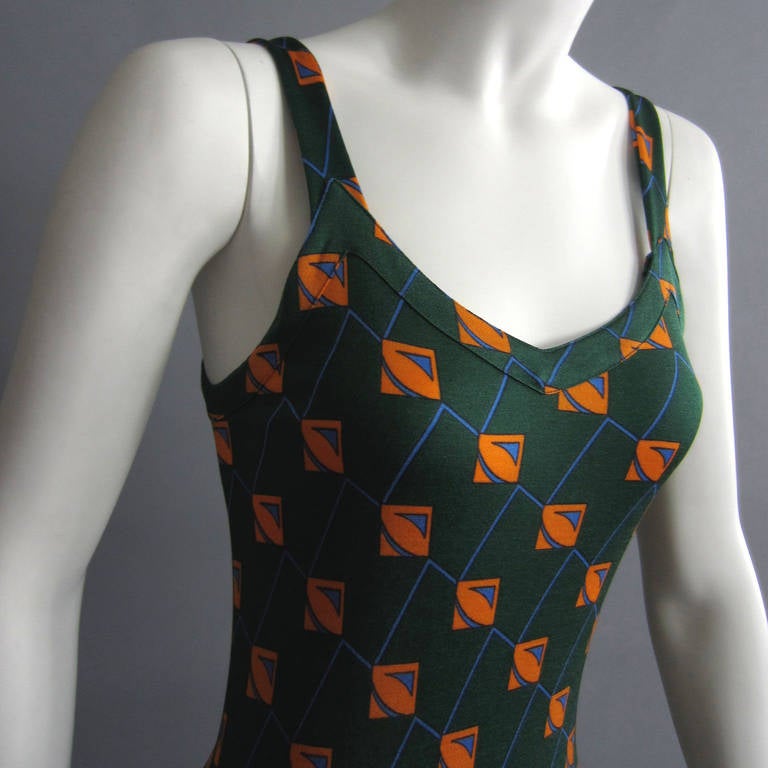 This 1970s maxi dress is fitted through the bodice and down through the hips. On the bottom, extra panels of fabric are sewn in to create fullness in the skirt; the dress flows with movement. The rich green serves as a backdrop to the orange and