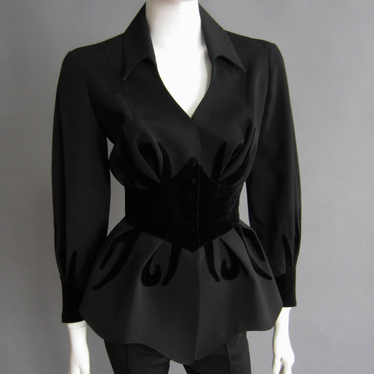 A fabulous piece of art by the master himself, THIERRY MUGLER. This black suit features a dramatic, fitted jacket and a pair of fitted, flared pants. The jacket features a velvet, corset style waistband with seam detailing. Along the front and back,