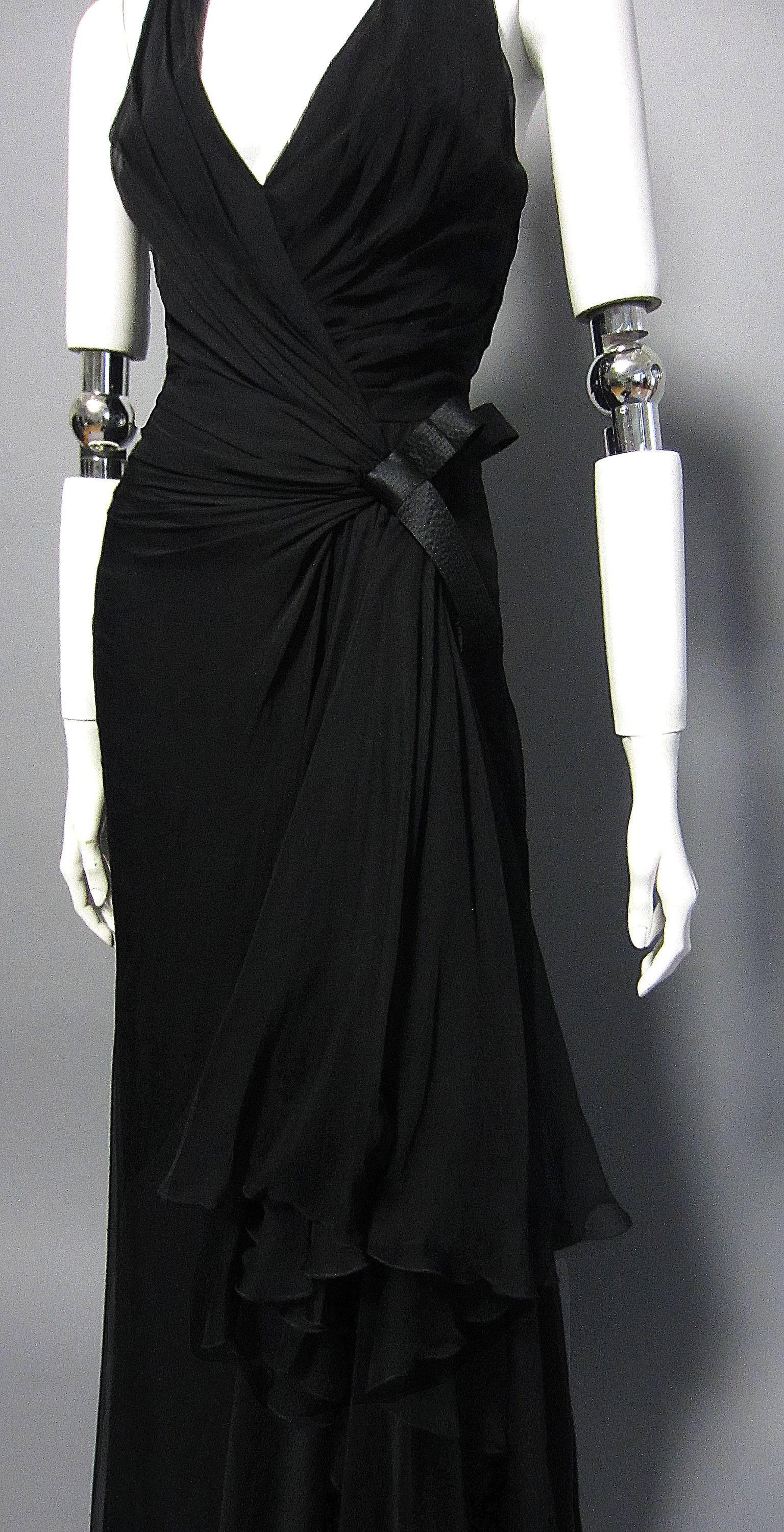 This VERSACE is sexy and sophisticated. The black chiffon is rushed along the bust, enhancing the halter shape of the neckline. The fabric gathers on the hip, where it is accented with a silk bow detail. From this point, extra panels of fabric fall
