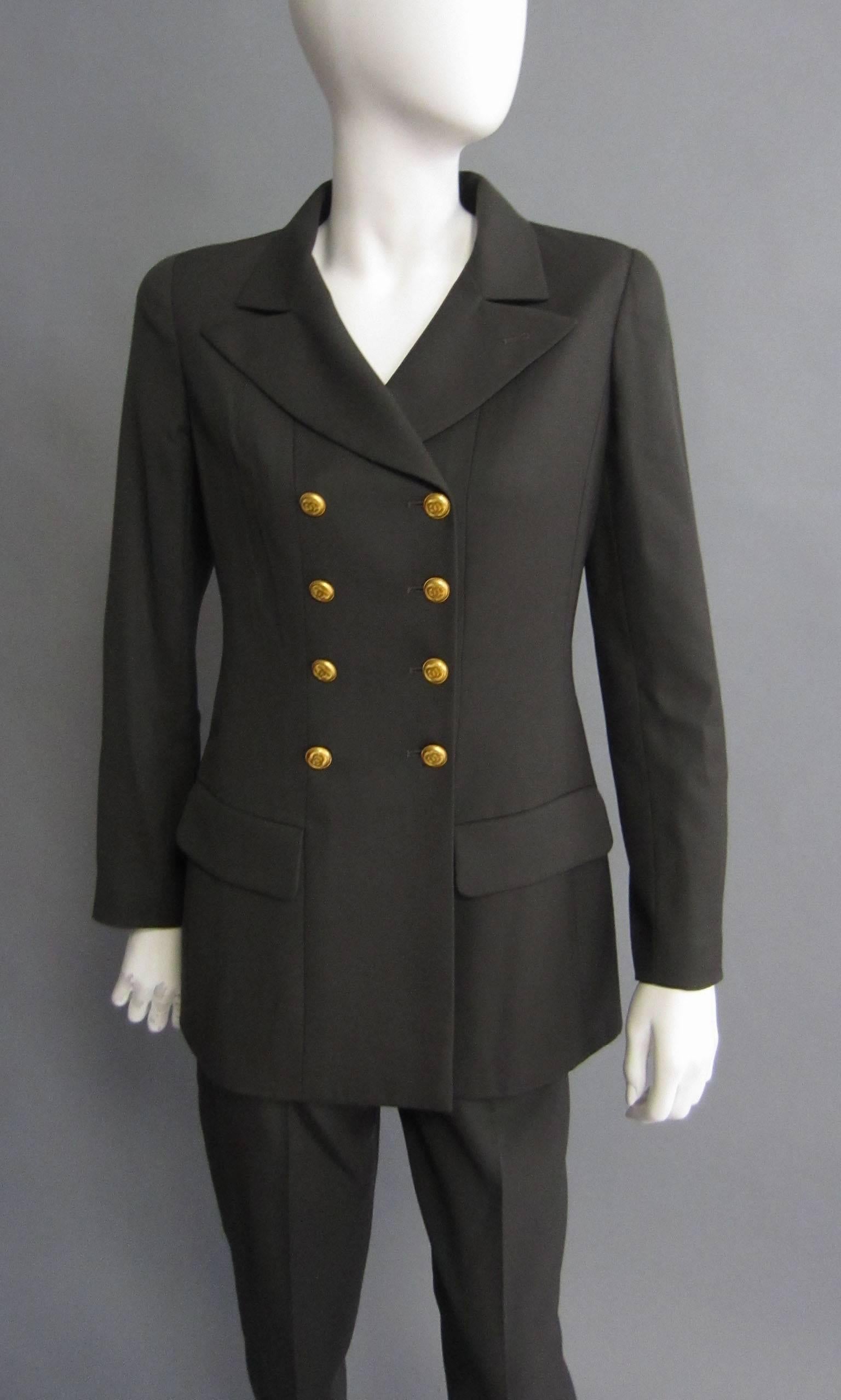 This CHANEL suit features a double breasted jacket and high waist pants. The jacket features two front pockets. The closure is accented with gold, CC logo buttons. The same buttons are repeated on the end of either sleeve. The same button secures